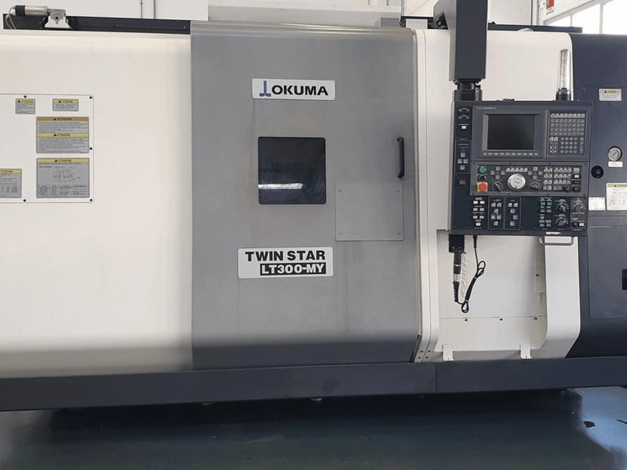 Okuma Twin Star LT300-MY CNC-Drehmaschine in der Seitenansicht, mit Bedienfeld, Bedientasten und Sicherheitsschildern.