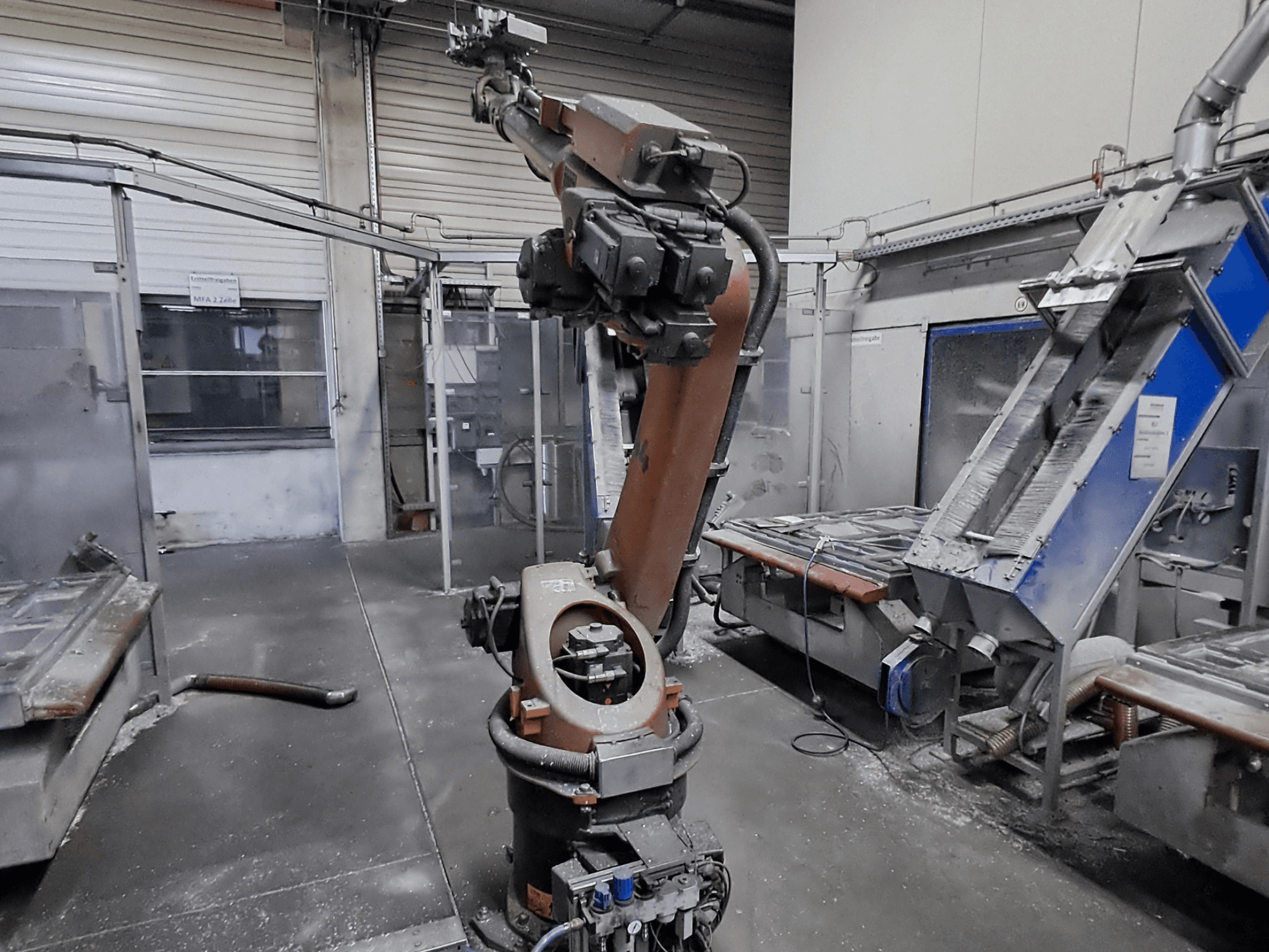 KUKA KR 30L16-2-Roboterarm in einer Werkstattumgebung, Vorderansicht, mit sichtbarem Staub und Maschinen im Hintergrund.