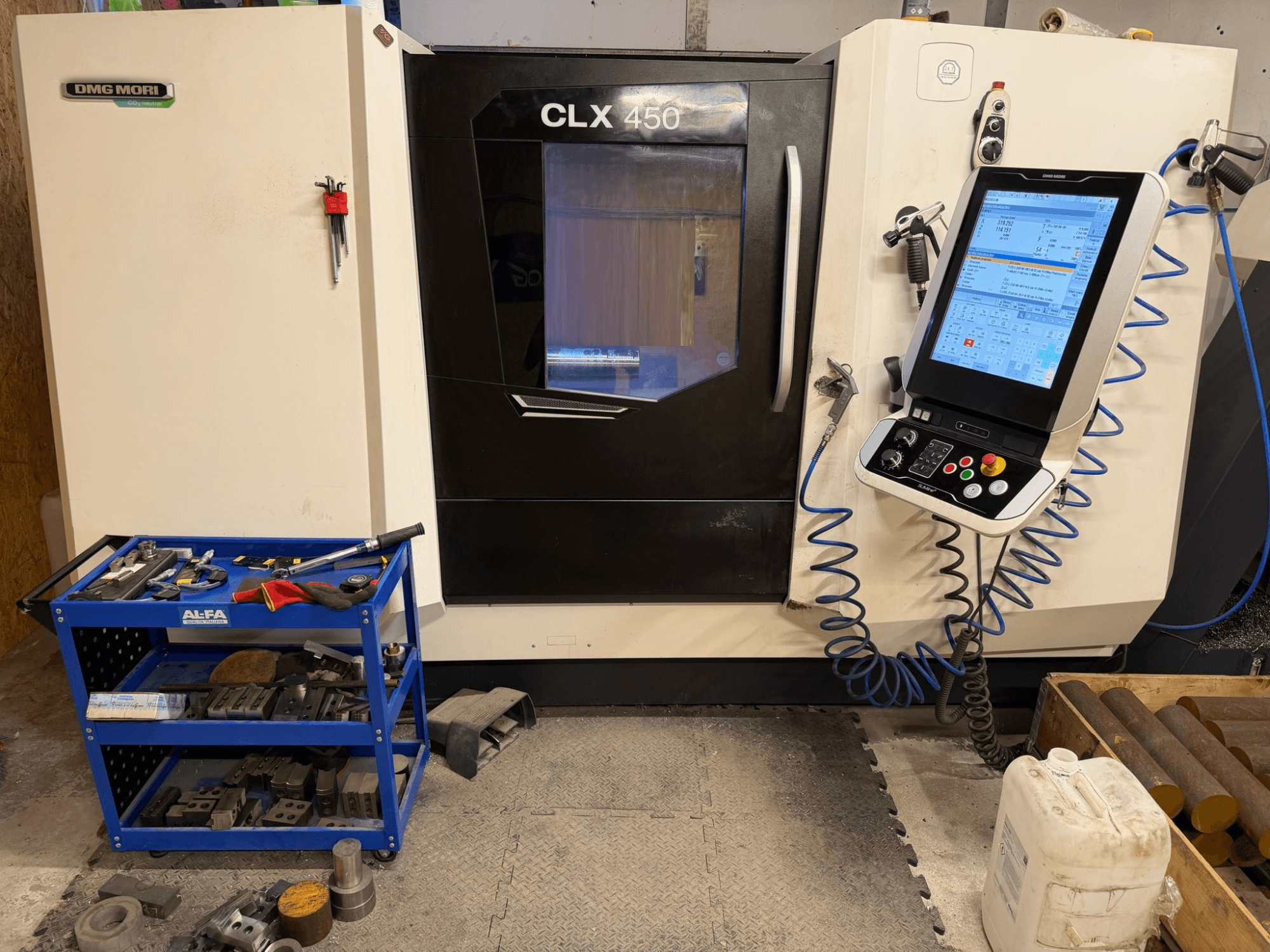 DMG MORI CLX 450 V3 Horizontal-Drehmaschine in der Frontansicht, mit Bedienfeld und Werkzeugwagen mit Ausrüstung.