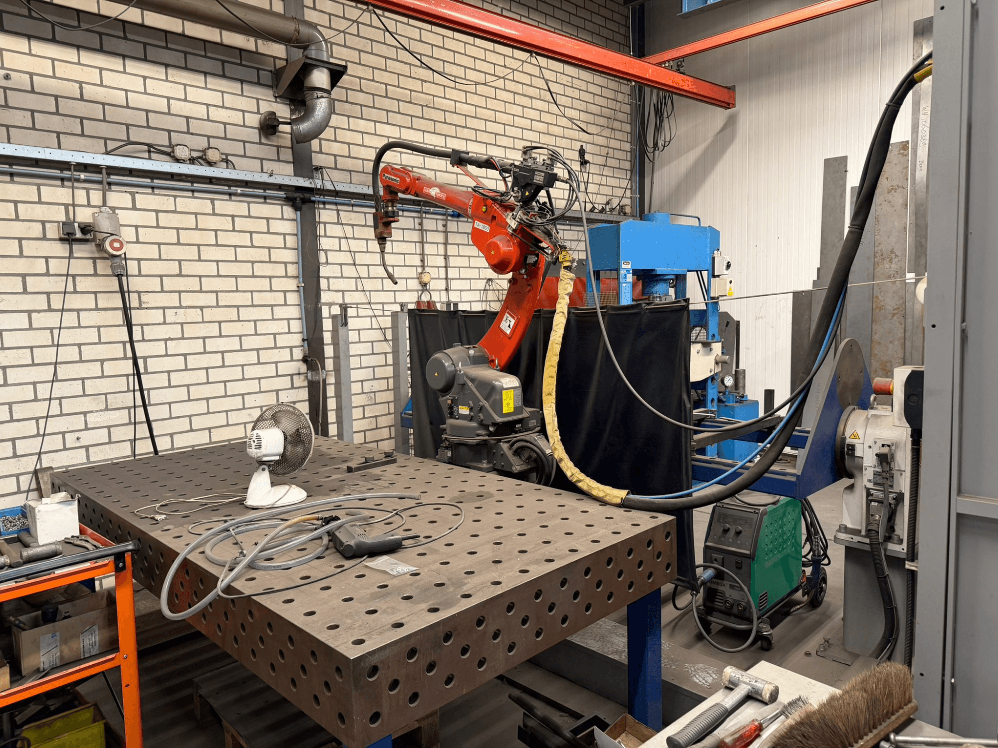 Vorderansicht eines PANASONIC TA-1800 Schweißroboters auf einer Arbeitsstation, mit einem Gebläse und einer Schweißausrüstung sichtbar.