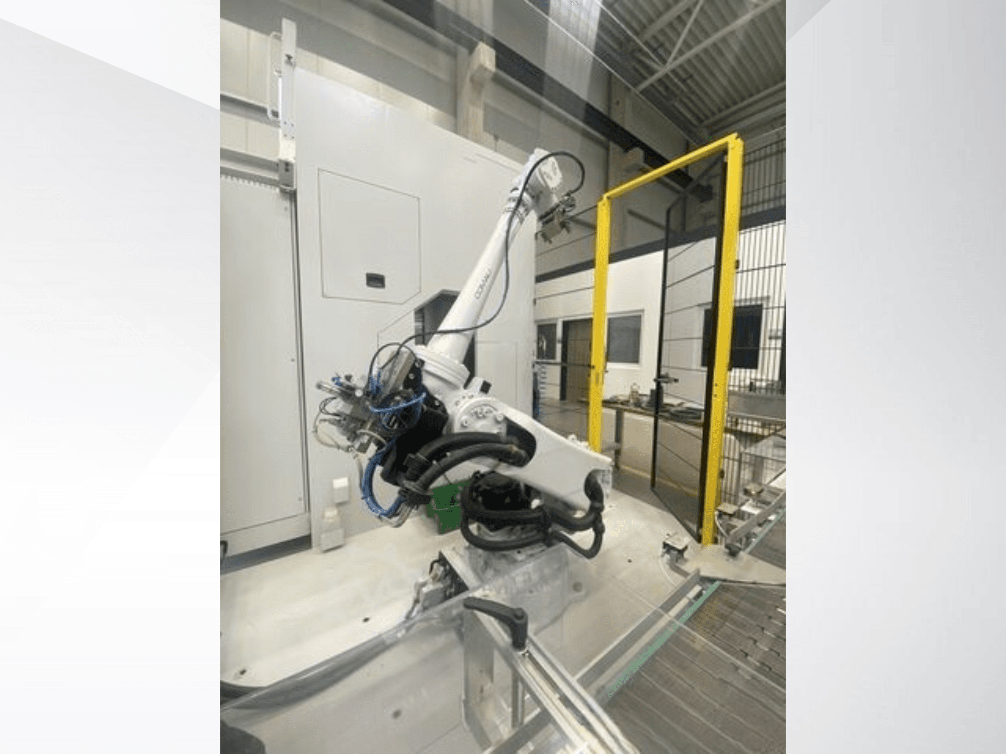 COMAU Smart NJ 40-2.5 Roboterarm in der Seitenansicht, mit Kabeln und gelber Sicherheitsschleuse in einer Fabrikumgebung.