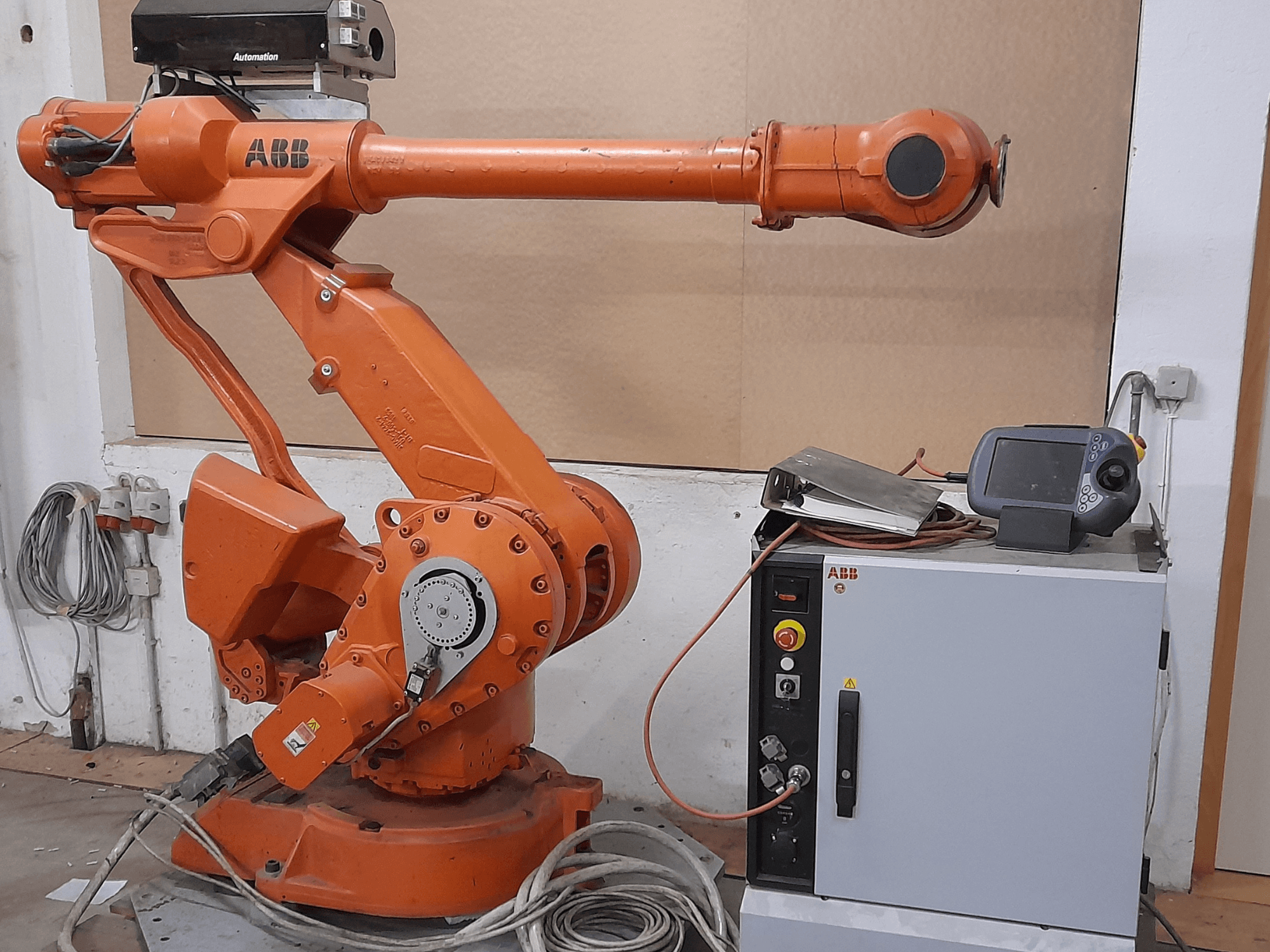 Orangefarbener ABB-Roboterarm mit Bedienfeld, Vorderansicht, mit Kabeln und Automatisierungsgeräten.