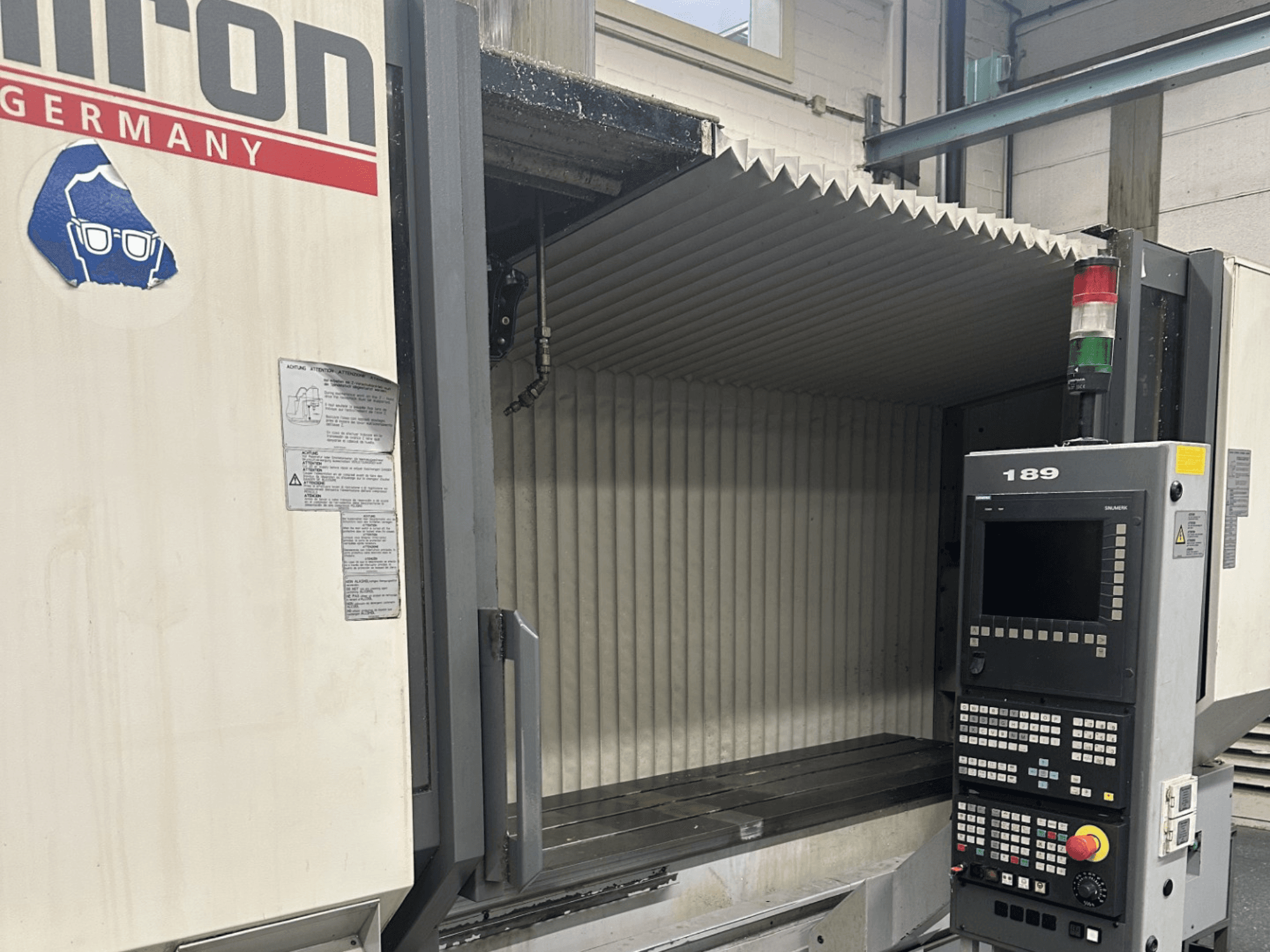 Alt-Text: Vorderansicht einer Hermle-CNC-Maschine mit einem Bedienfeld mit Tasten und einem Display, das einen offenen Arbeitsbereich aufweist.