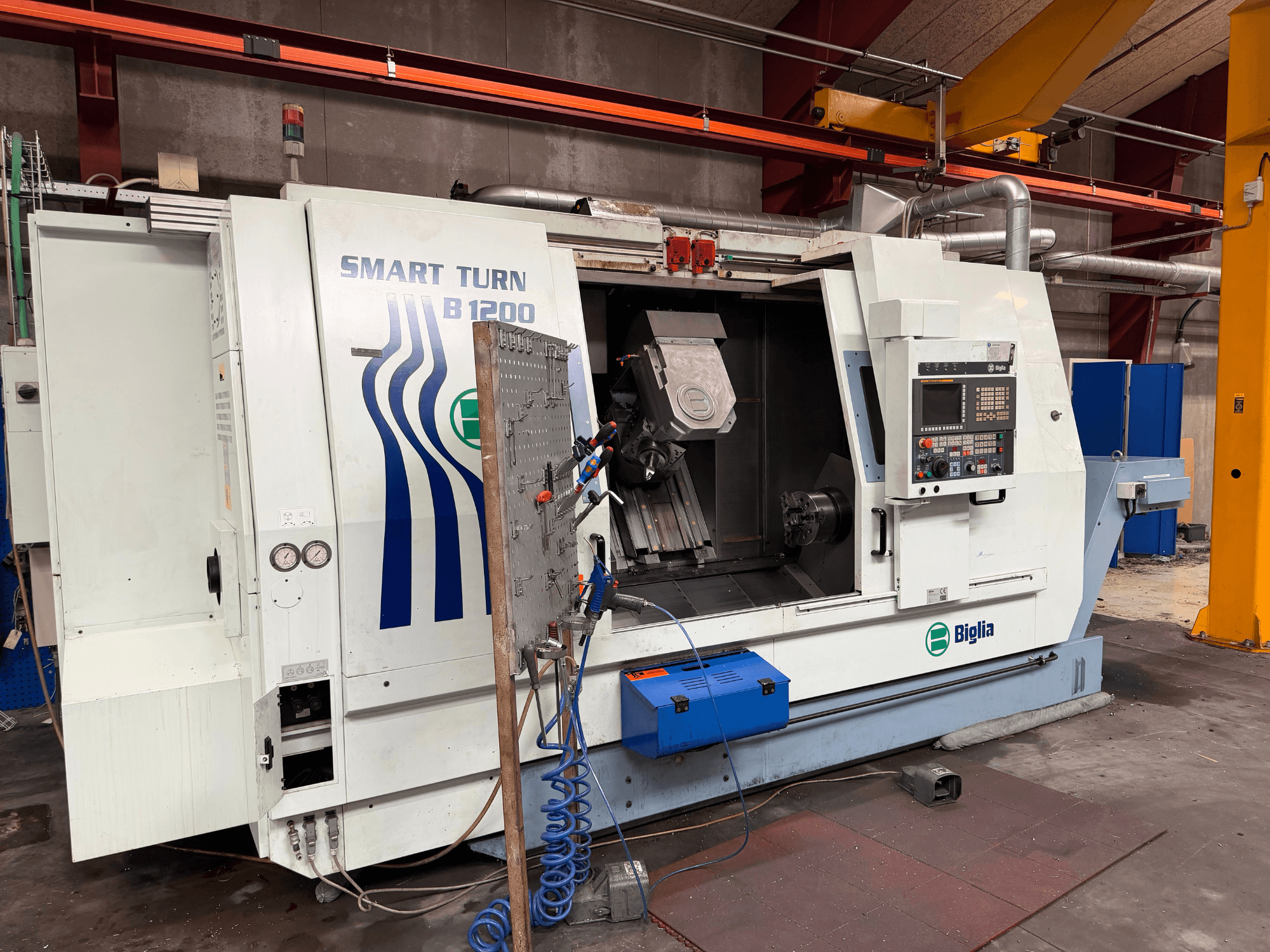 Dreh-Fräszentrum Biglia B.1200/S-Smart in der Vorderansicht; zu sehen sind die Bedienelemente, ein Werkstück in der Spindel und Manometer.