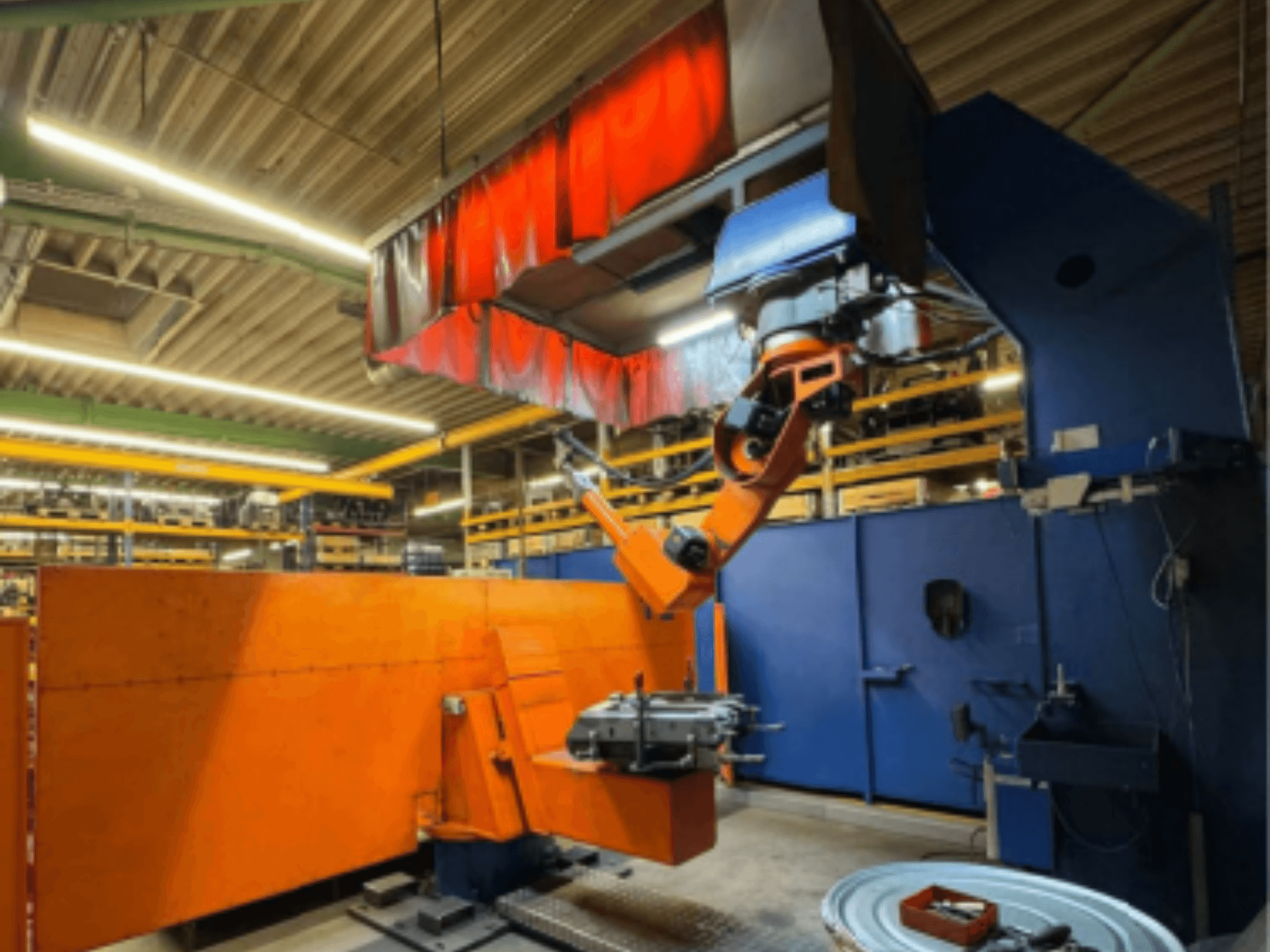 CLOOS Romat 350 e Schweißroboter in einer industriellen Umgebung, Frontansicht mit orangefarbenem Arm, der ein Werkstück unter einem Deckenvorhang hält.