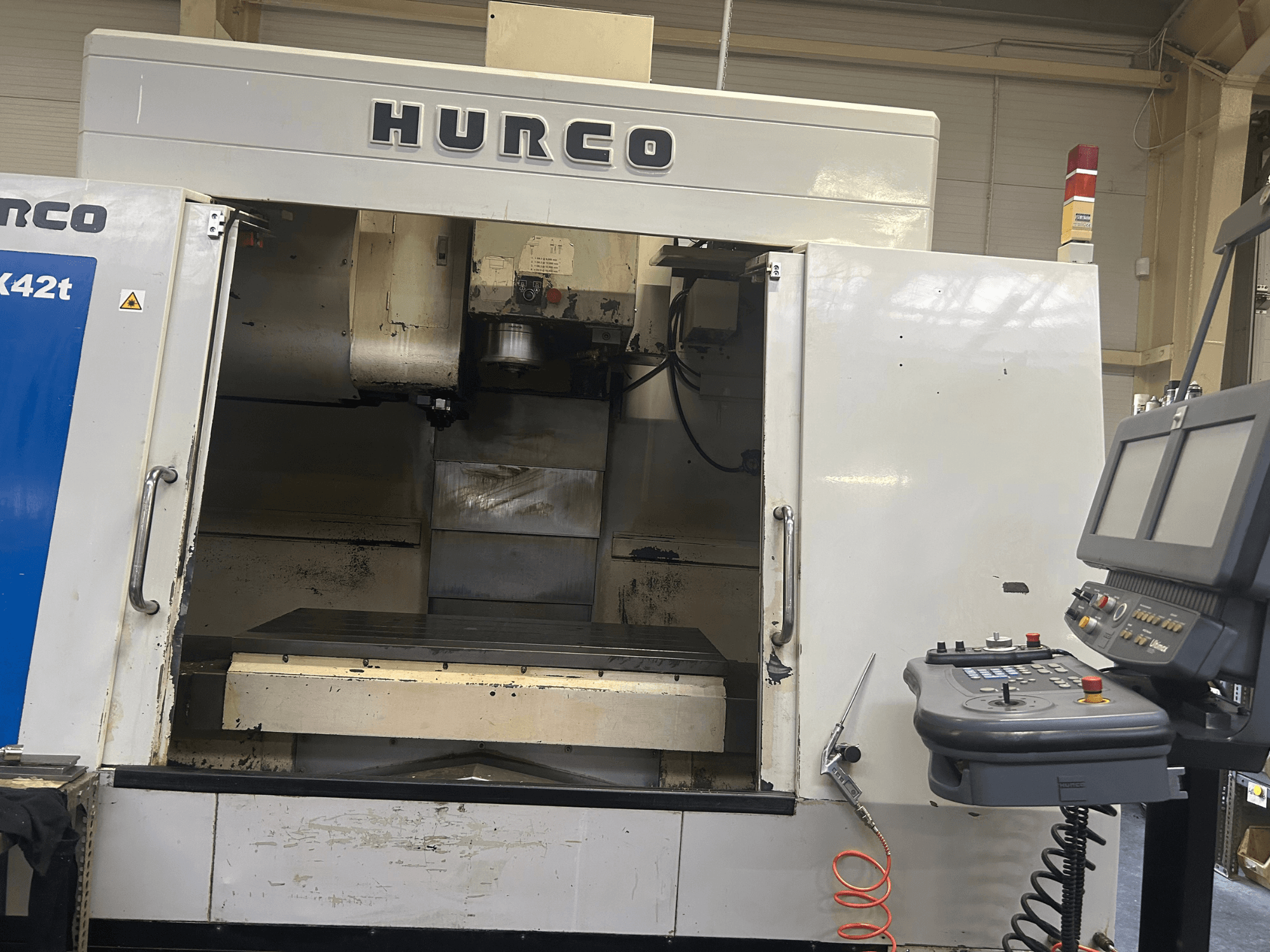 Hurco VMX42T CNC-Fräsmaschine in der Vorderansicht, mit offenem Arbeitsbereich und Bedienfeld mit Tasten und Display.