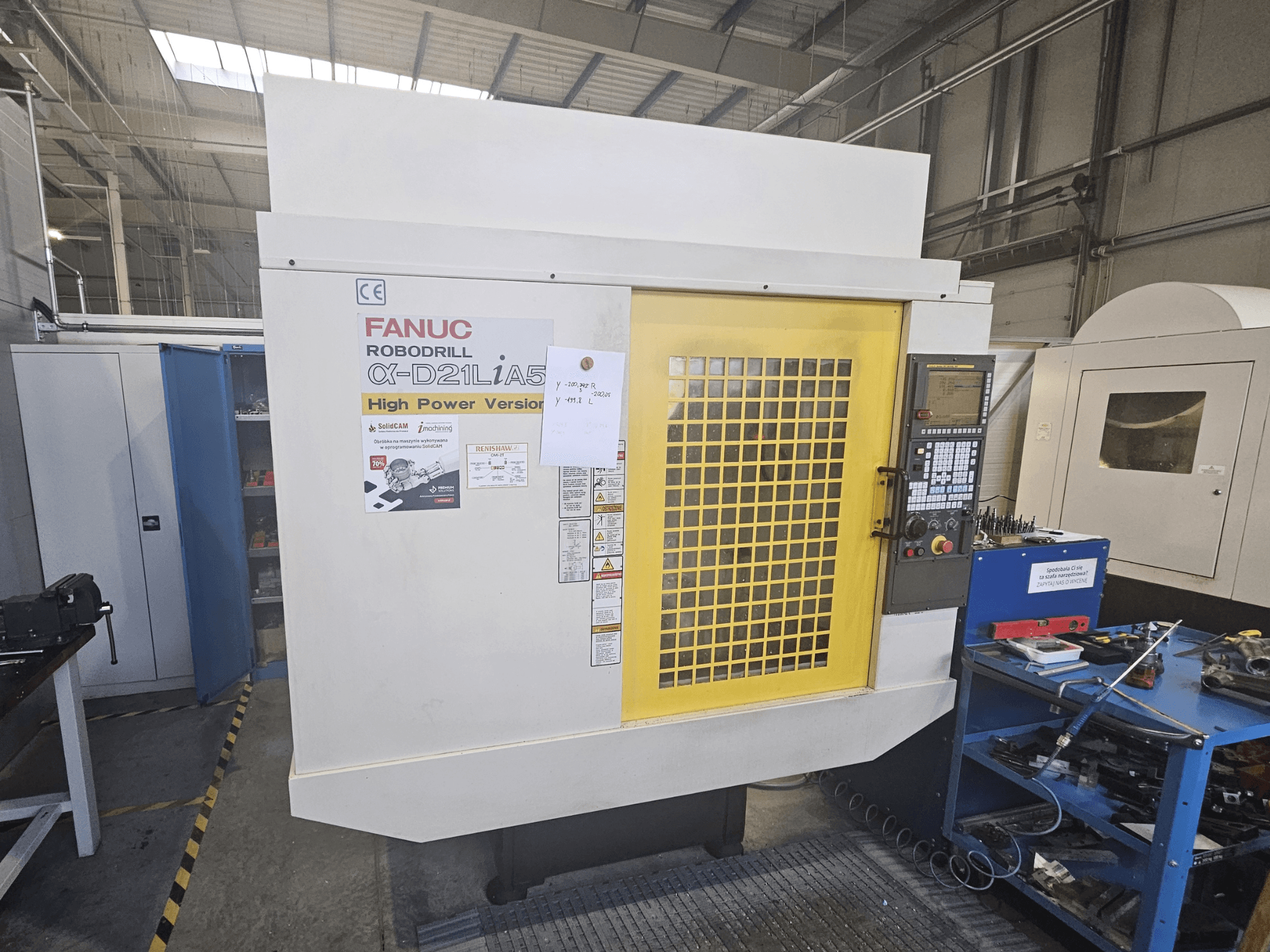 Vorderansicht eines FANUC Robodrill α-D21LiA5 mit gelber Schutztür, Bedienfeld und Werkzeugen im Arbeitsbereich.