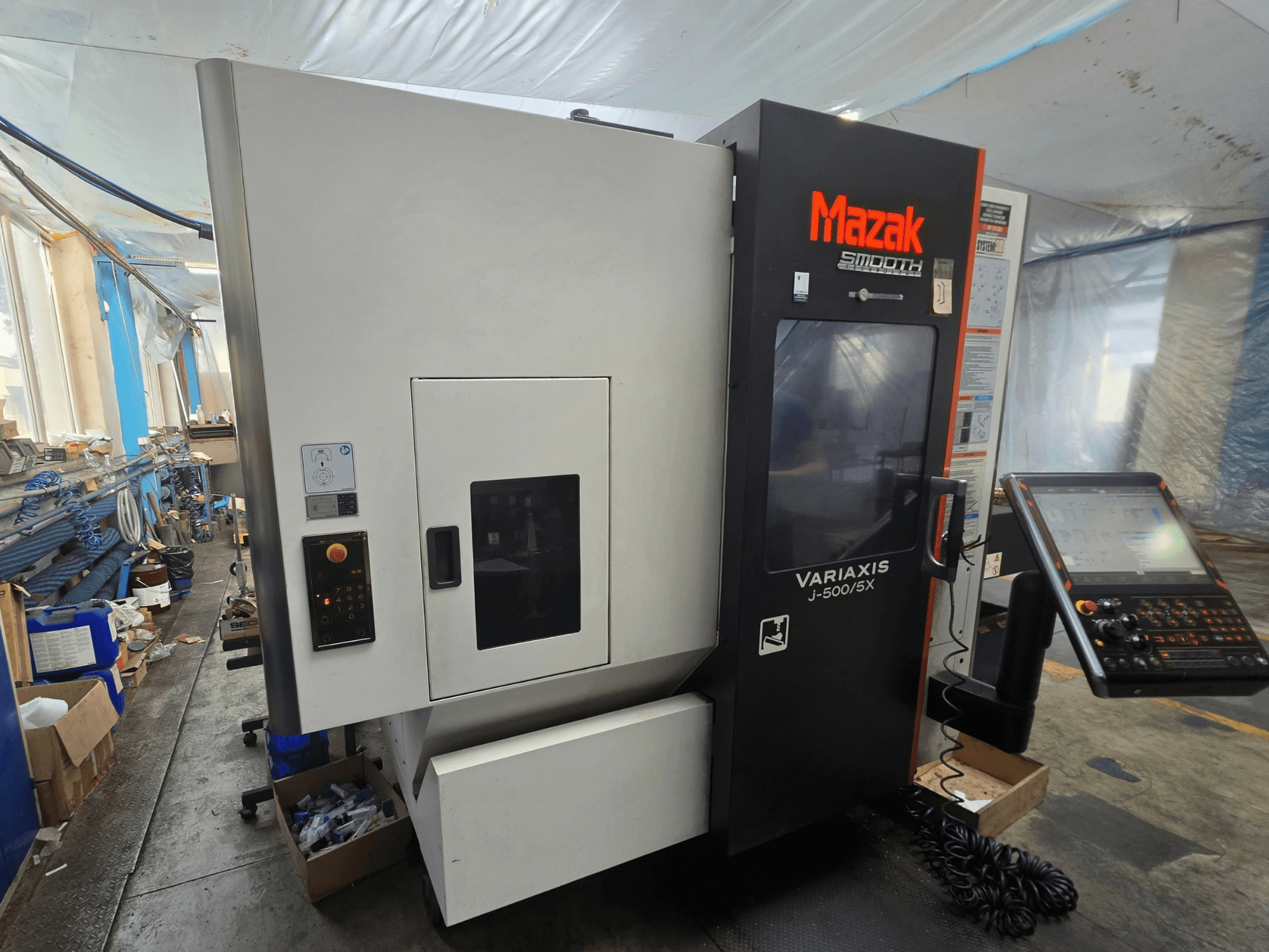 Vertikales Bearbeitungszentrum Mazak VARIAXIS J-500/5X, Seitenansicht mit Bedienelementen und Display, in einer Werkstattumgebung.