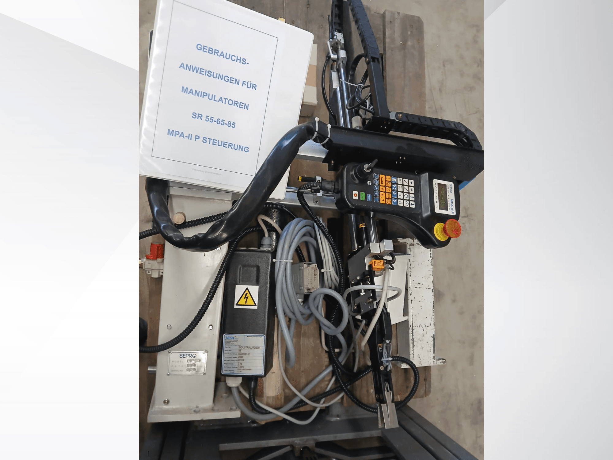 Bedienfeld und Komponenten des Sepro PIP-55 Portalroboters, von der Seite betrachtet, mit sichtbarem Benutzerhandbuch.