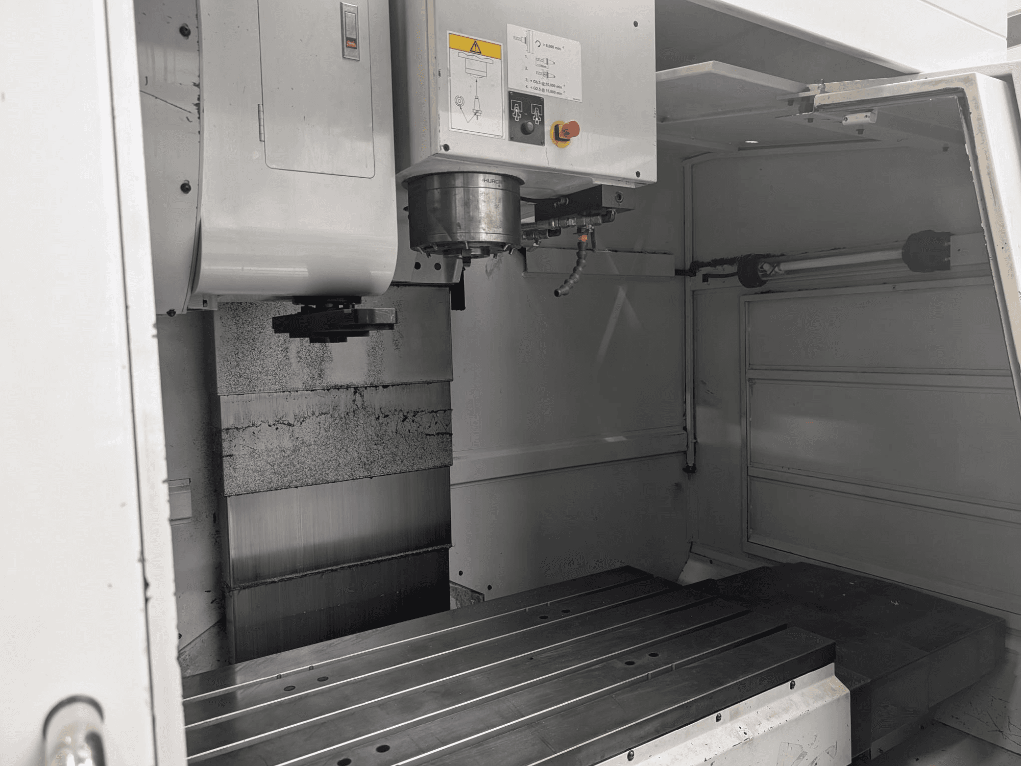 Innenansicht einer CNC-Fräsmaschine mit großem Metallarbeitstisch und Spindelmotor, mit detaillierten Komponenten und Bedienfeld.