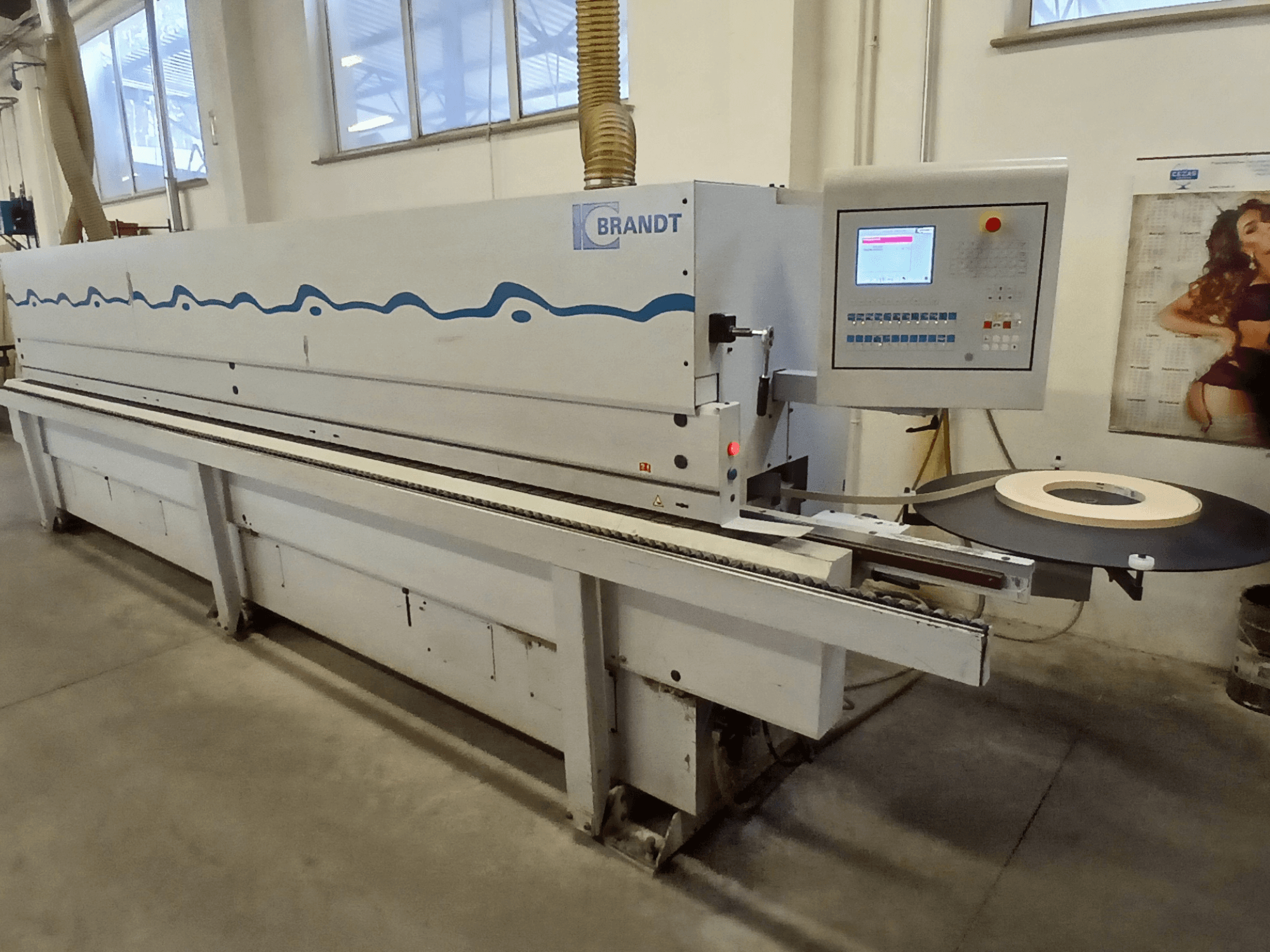 Brandt-Kantenanleimmaschine, Seitenansicht, mit Bedienfeld und einer Bandrolle auf dem Zuführtisch.