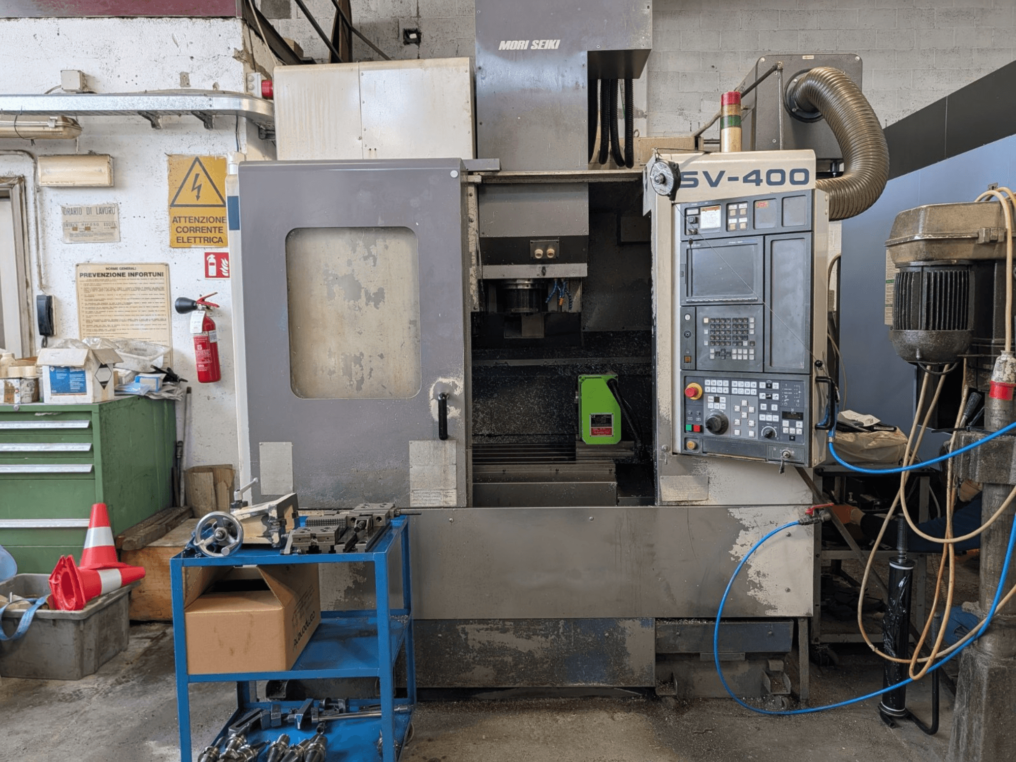 MORI SEIKI SV-400 Vertikal-Bearbeitungszentrum in einer Werkstatt, Seitenansicht, mit Bedienfeld und Werkzeugmaschinen daneben.
