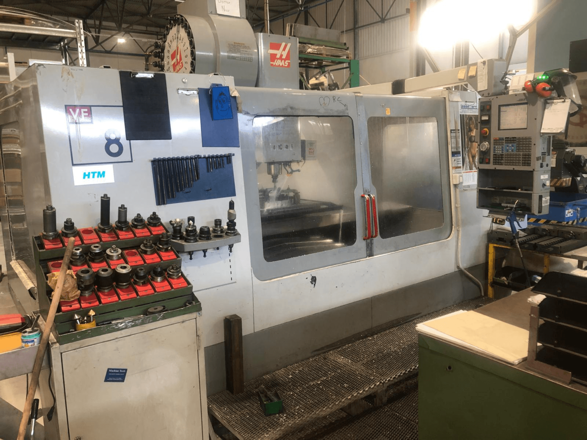 Haas CNC-Maschine in einer Werkstatt, Vorderansicht; zeigt Werkzeuge und Bedienelemente, mit sichtbaren Modelldetails und organisierten Werkzeughaltern.