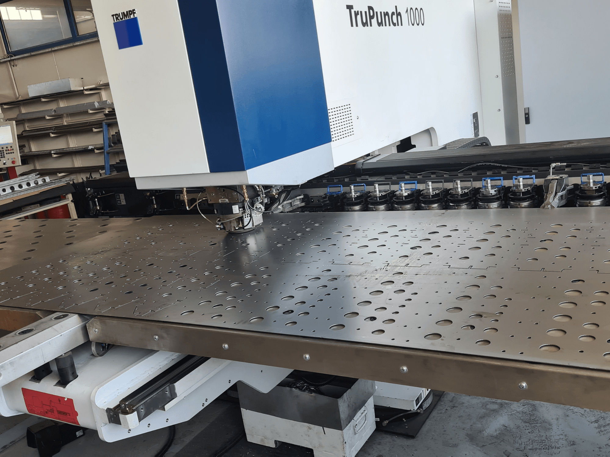 CNC-Stanzmaschine TRUMPF TruPunch 1000, Vorderansicht, mit einem Lochblech und der Werkzeugbestückung.