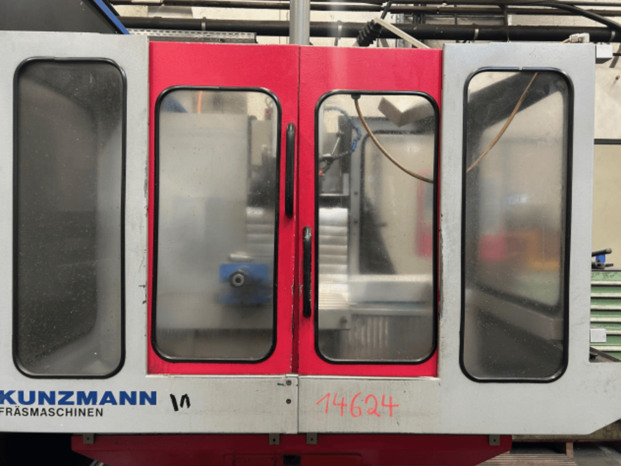 Frontansicht der CNC-Maschine von KUNZMANN, mit roten und grauen Platten, mit sichtbarem Bedienfeld und Werkzeughalter im Inneren.