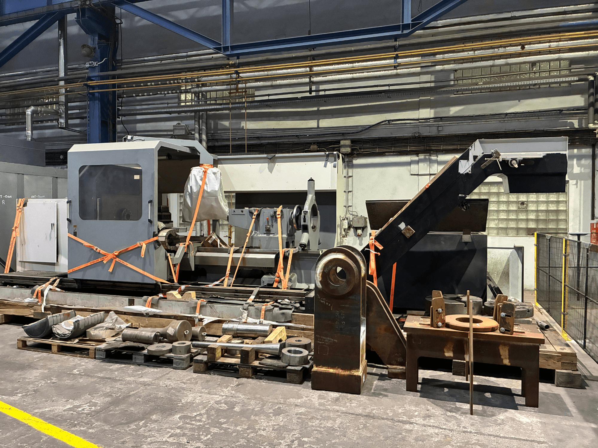 Die Horizontal-Drehmaschine Geminis GT5 G2-1000x2000 in der Vorderansicht, mit Gurten gesichert und von verschiedenen Geräten umgeben.