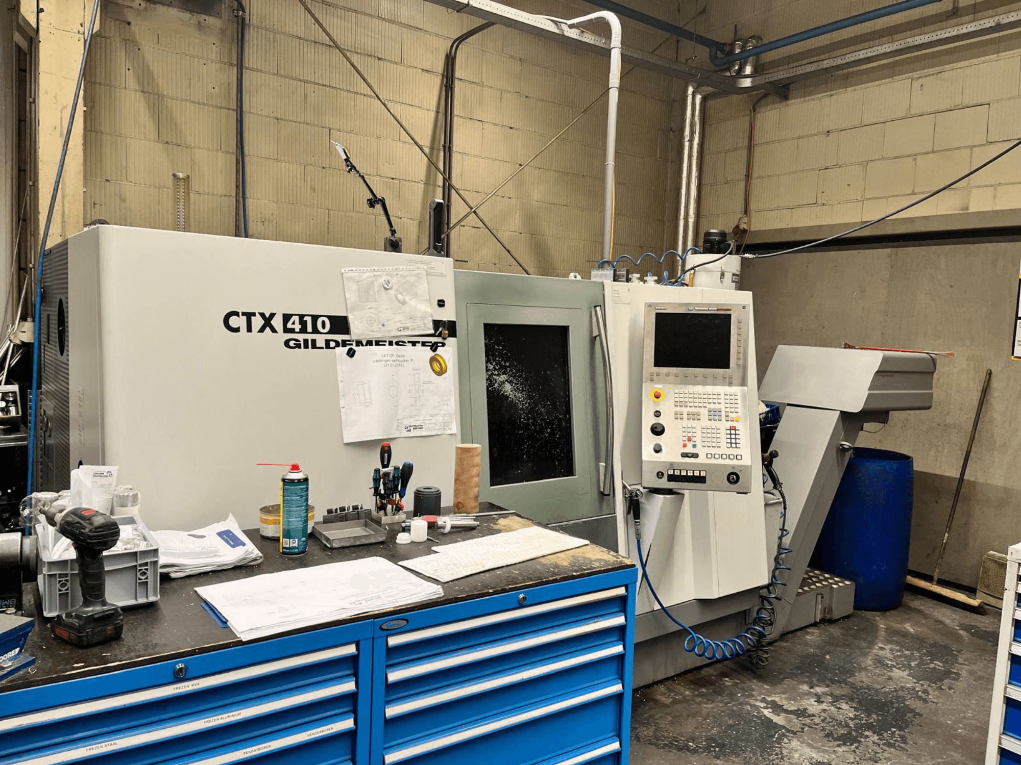 Gildemeister CTX 410 CNC-Maschine in einer Werkstatt, Vorderansicht, mit einem Bedienfeld und verschiedenen Werkzeugen auf einer Werkbank.