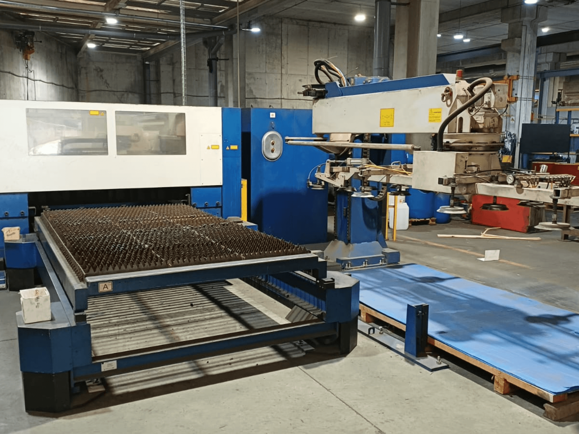 TRUMPF TRUMATIC L 3030 CO₂-Laserschneidmaschine, Seitenansicht, die den Schneidtisch mit genoppter Oberfläche und Roboterarm zeigt.