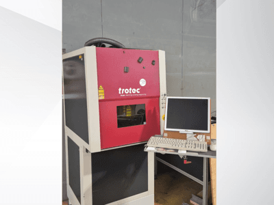 Rote Trotec-Laser-Work-Station von vorne gesehen, mit Monitor und Tastatur auf einem Arbeitstisch.
