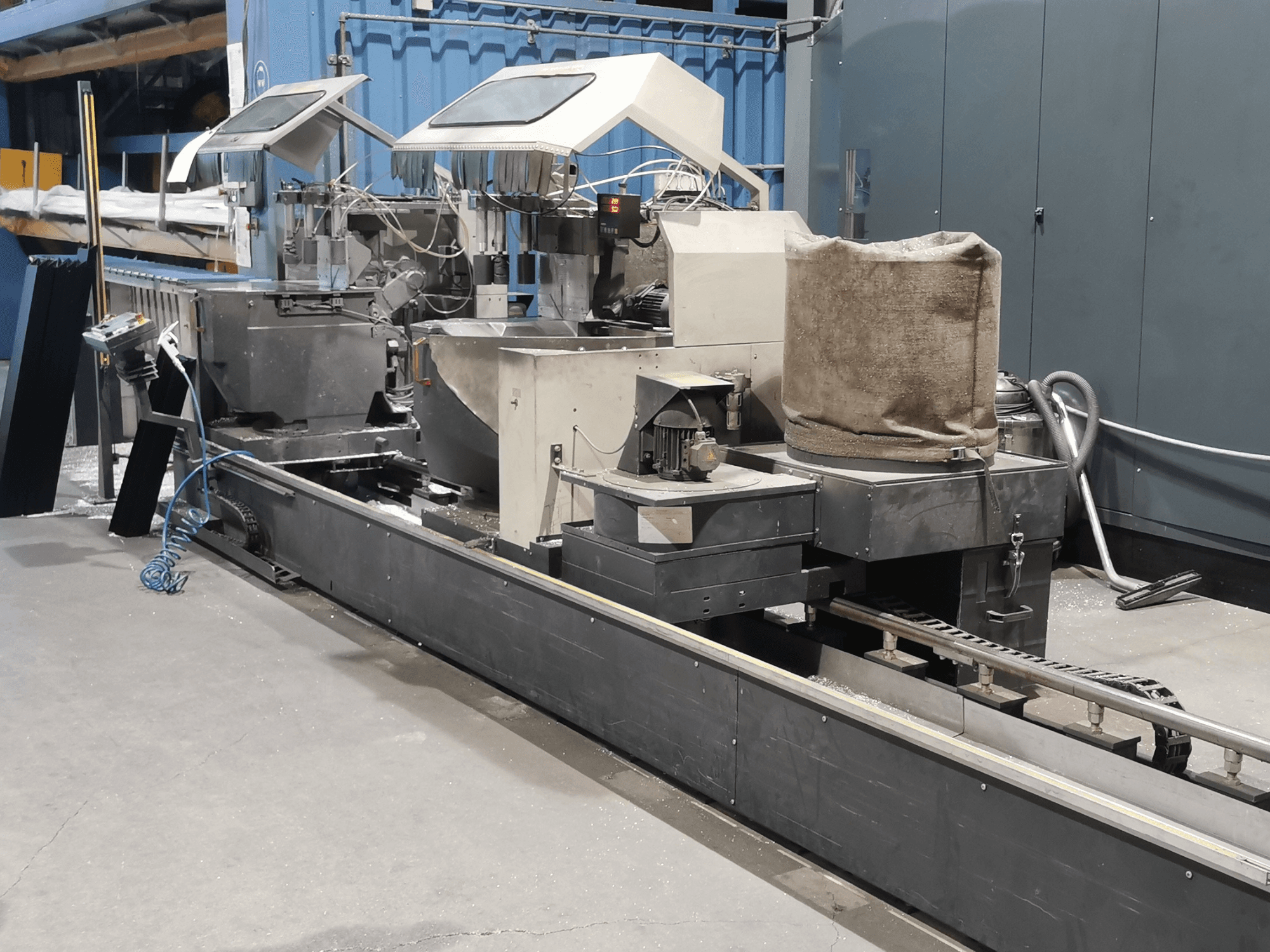 Industrielle Verarbeitungsmaschine in der Seitenansicht mit Trichtern, Förderband und Bedienfeld in einer Fabrikumgebung.