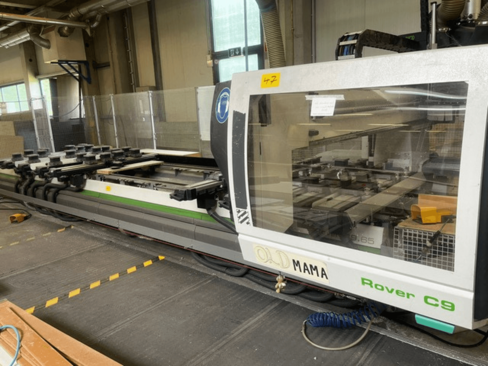 BIESSE Rover C 9.65 CNC-Oberfräse in einer Werkstatt, Seitenansicht mit Bedienfeld und Arbeitstisch mit Klemmen.