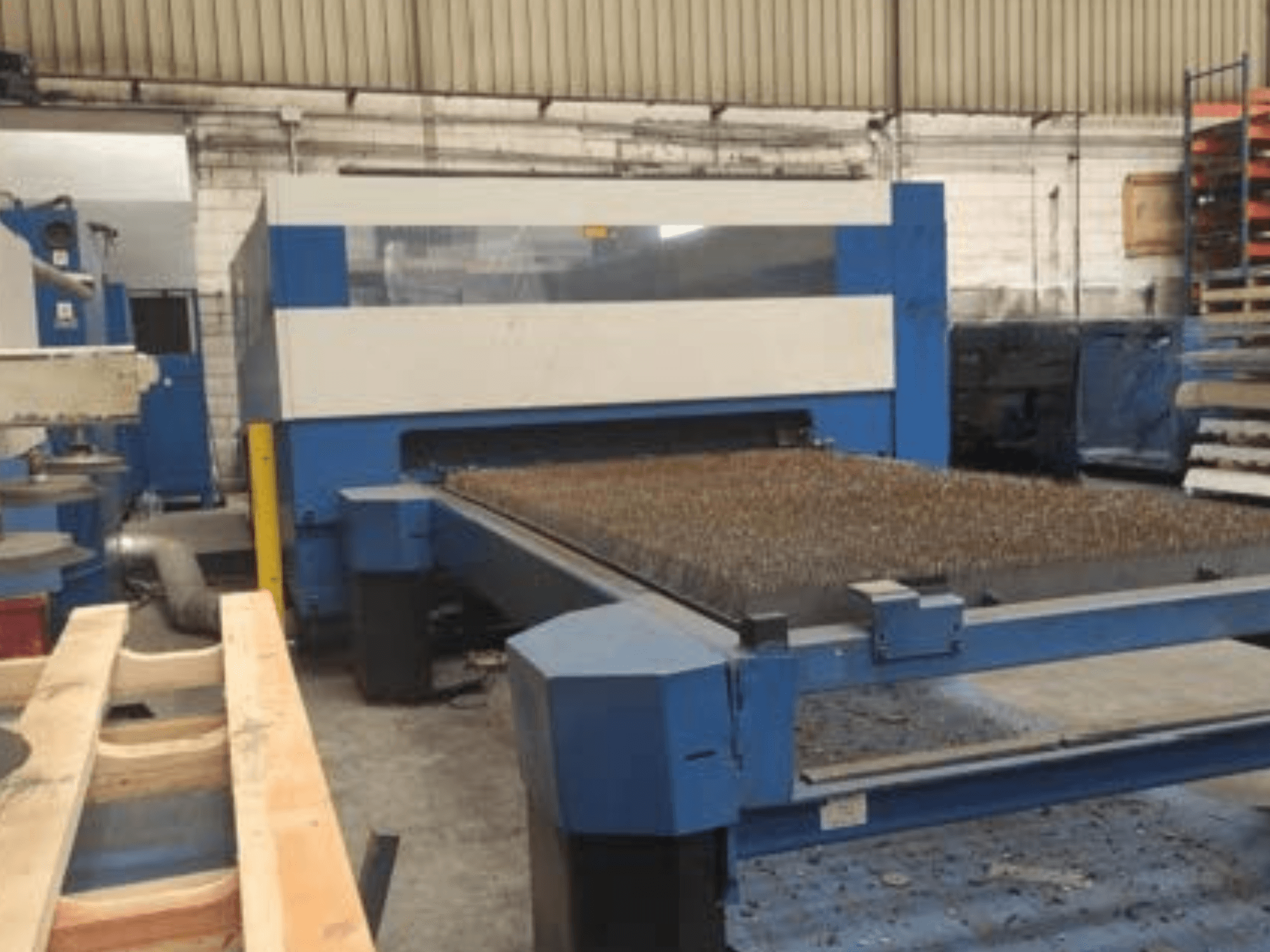 Blaue Laserschneidmaschine mit einem strukturierten Metallbett, Seitenansicht, zeigt die Betriebseinrichtung in einem industriellen Arbeitsbereich.