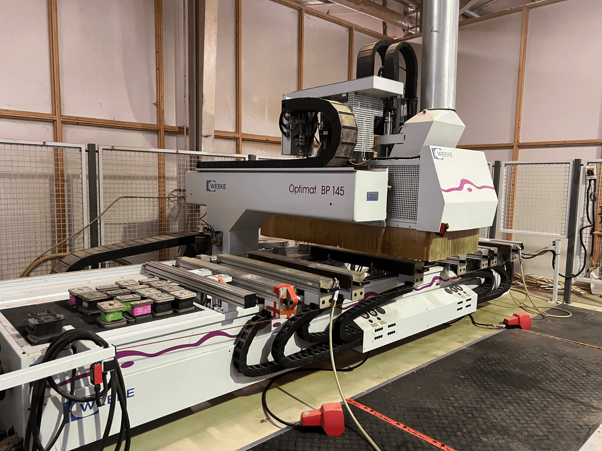 WEEKE Optimat BP 145 in einer Fabrik, die eine CNC-Maschine mit Bedientasten und Kabeln zeigt, von der Seite gesehen.
