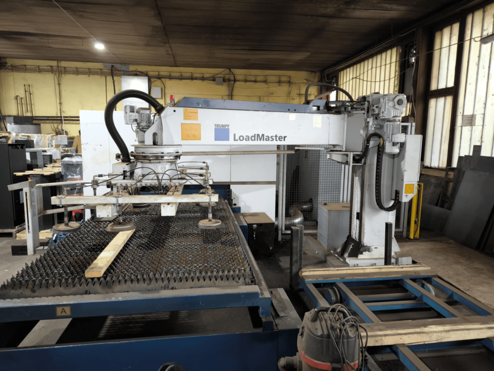 TRUMPF TRULASER 3030 FIBER Schneidmaschine, Frontansicht, mit LoadMaster System und auf einem gerasterten Arbeitstisch positioniert.