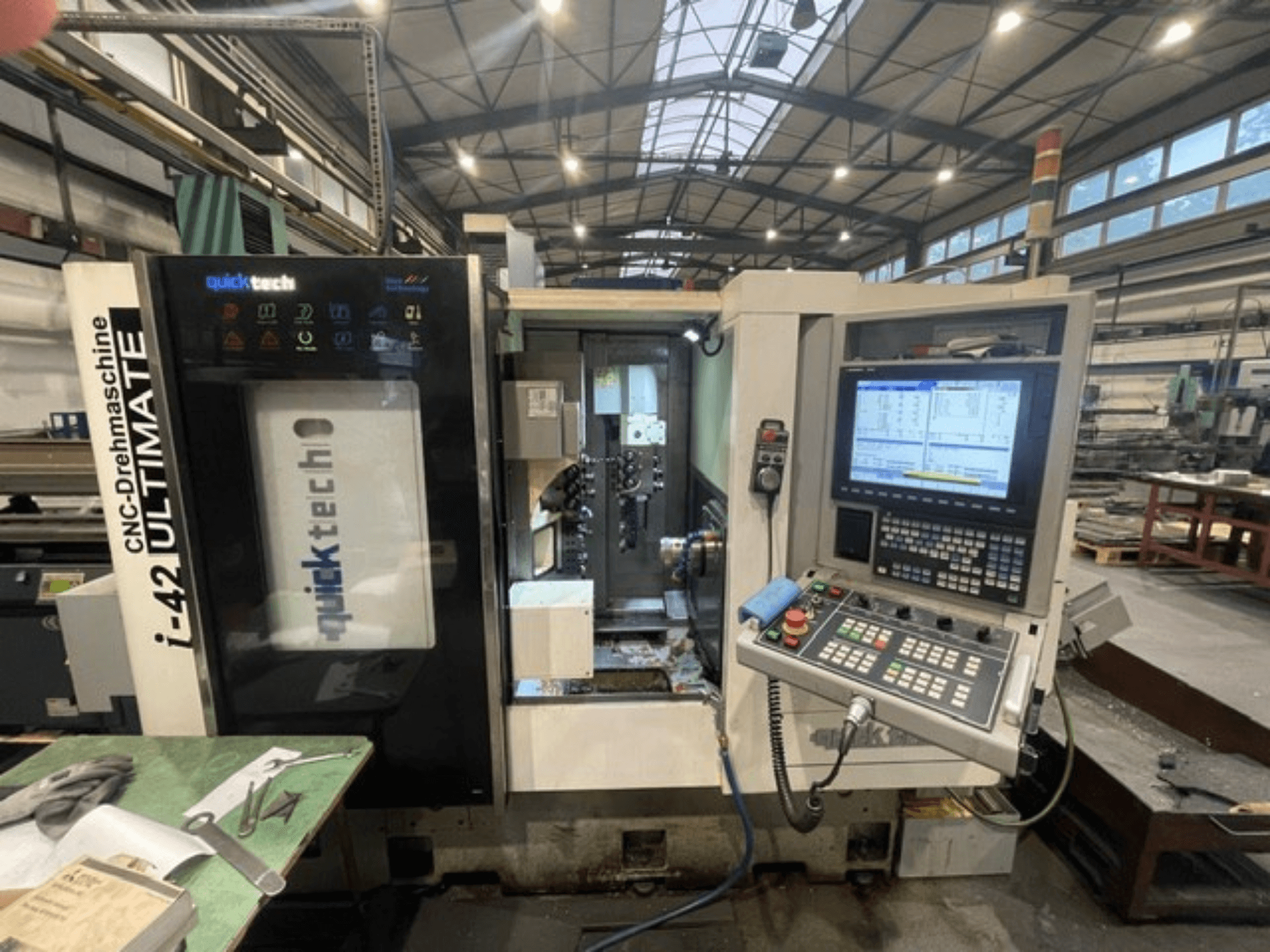 Quick-Tech I-42U Schweizer Drehmaschine, Vorderansicht, zeigt das Bedienfeld und die CNC-Schnittstelle in einer Werkstattumgebung.