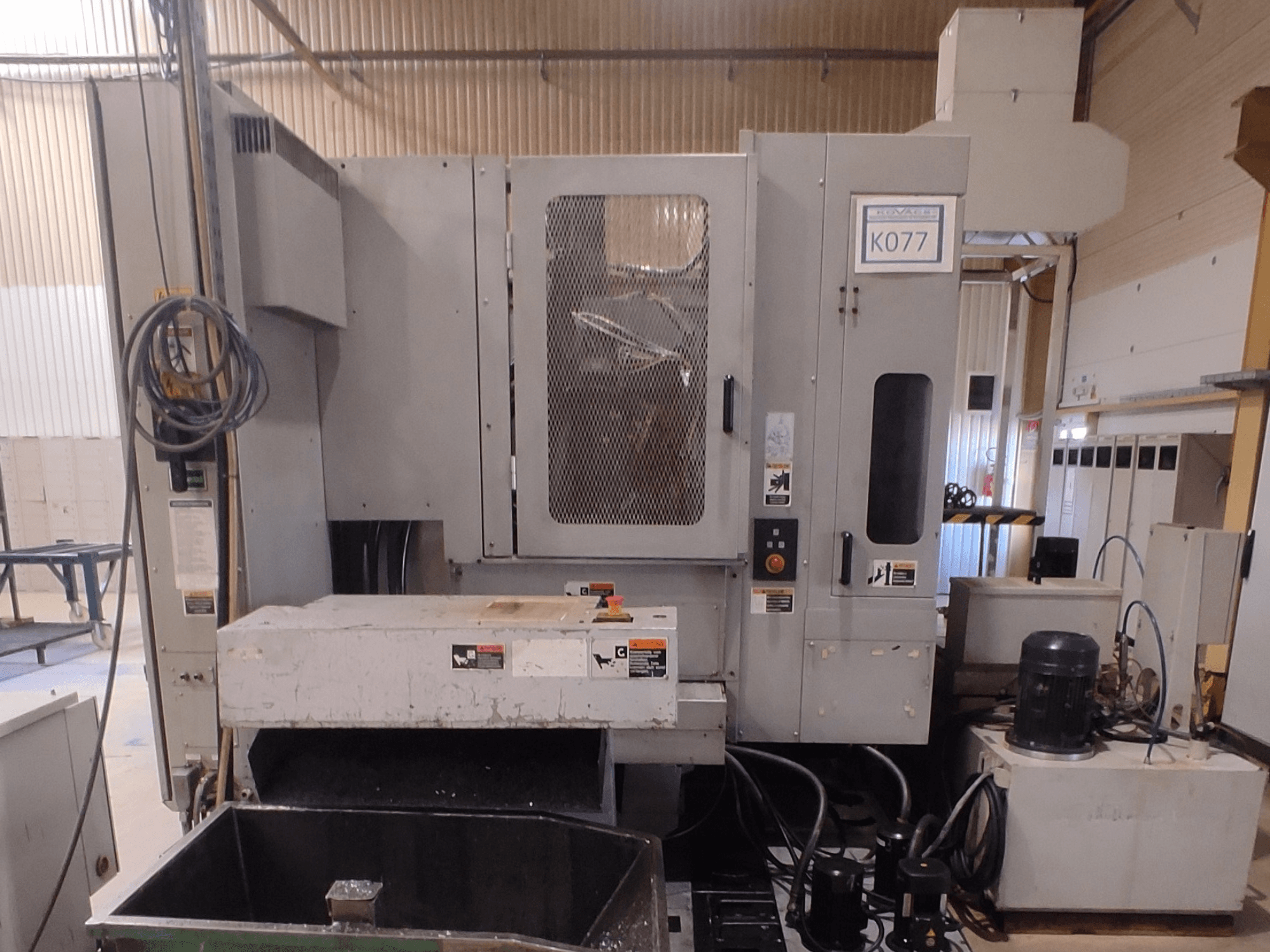 Graue CNC-Industriemaschine mit großem Arbeitstisch, Seitenansicht, mit Bedienfeld und Kühlmittelbehälter, Modell K077.