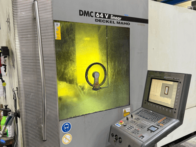 DMC 64 V linear von Deckel Maho, Vorderansicht der Maschine mit Bedienfeld und gelb getöntem Fenster, das die inneren Mechanismen zeigt.