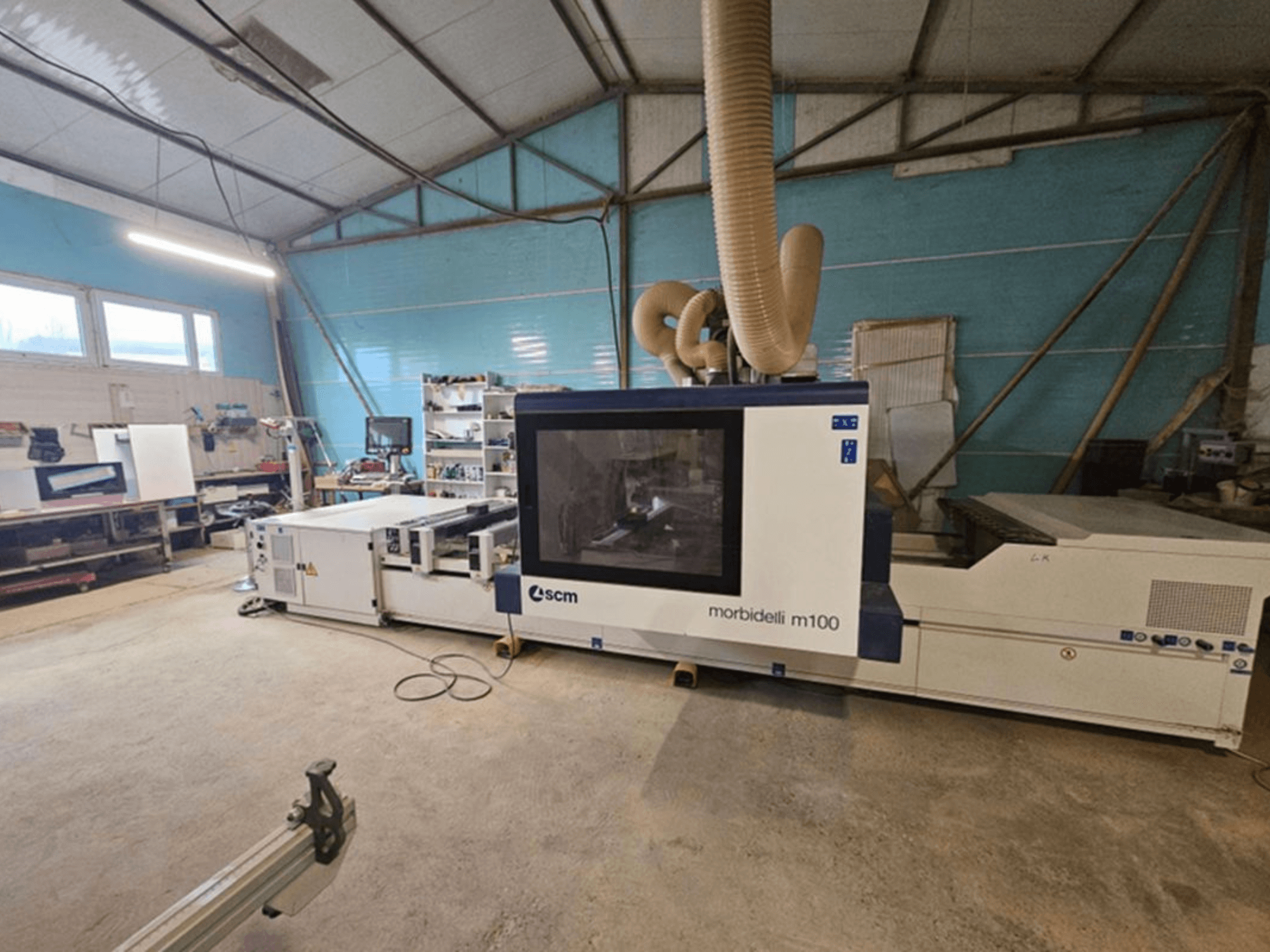 CNC-Bearbeitungszentrum SCM MORBIDELLI M 100 in einer Werkstatt, Vorderansicht mit Staubabsaugung und der umgebenden Arbeitsplatzausstattung.