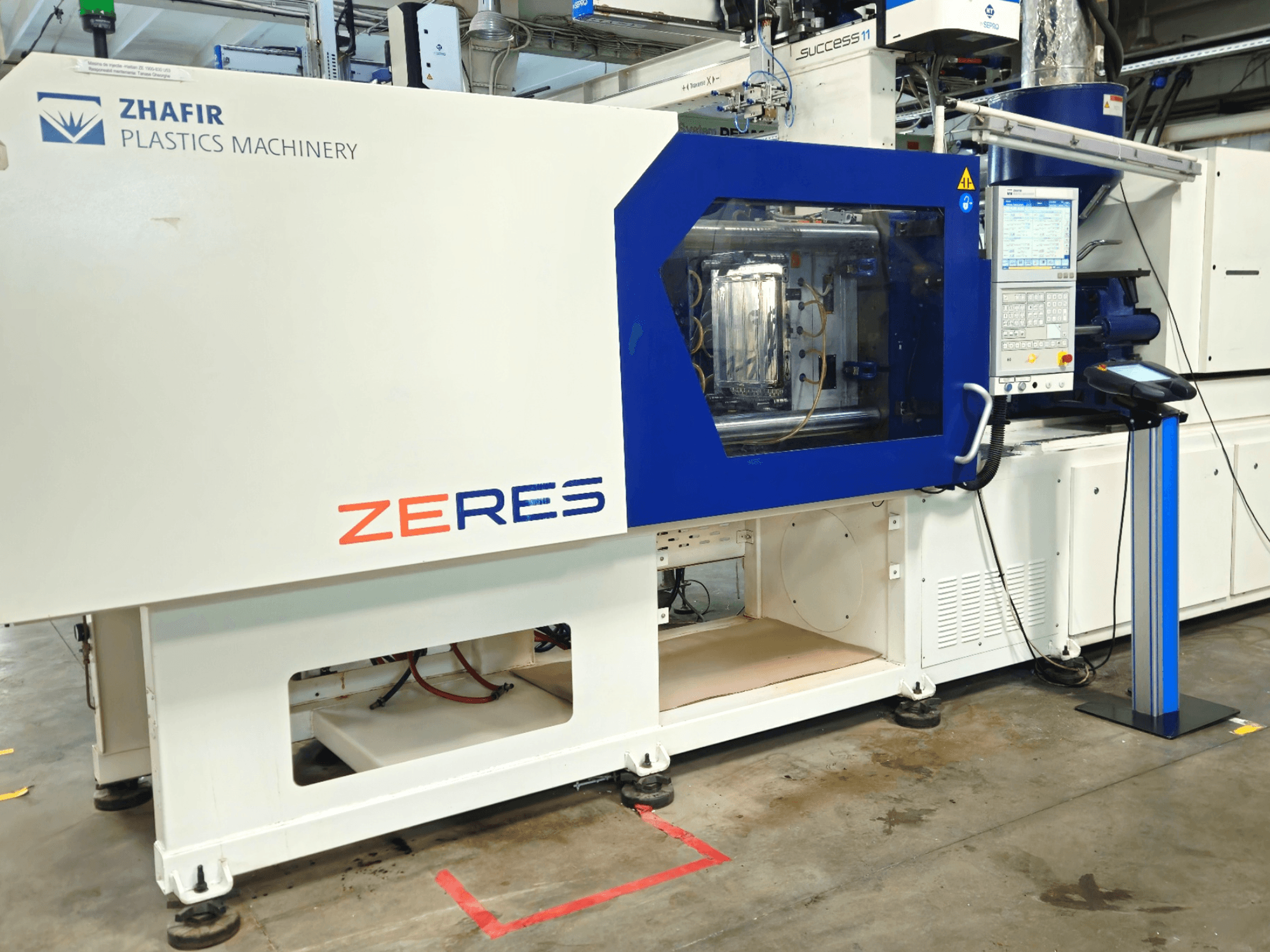 Zhafir Zeres-Spritzgießmaschine in der Vorderansicht, mit Bedienfeld und transparentem Formteilbereich.