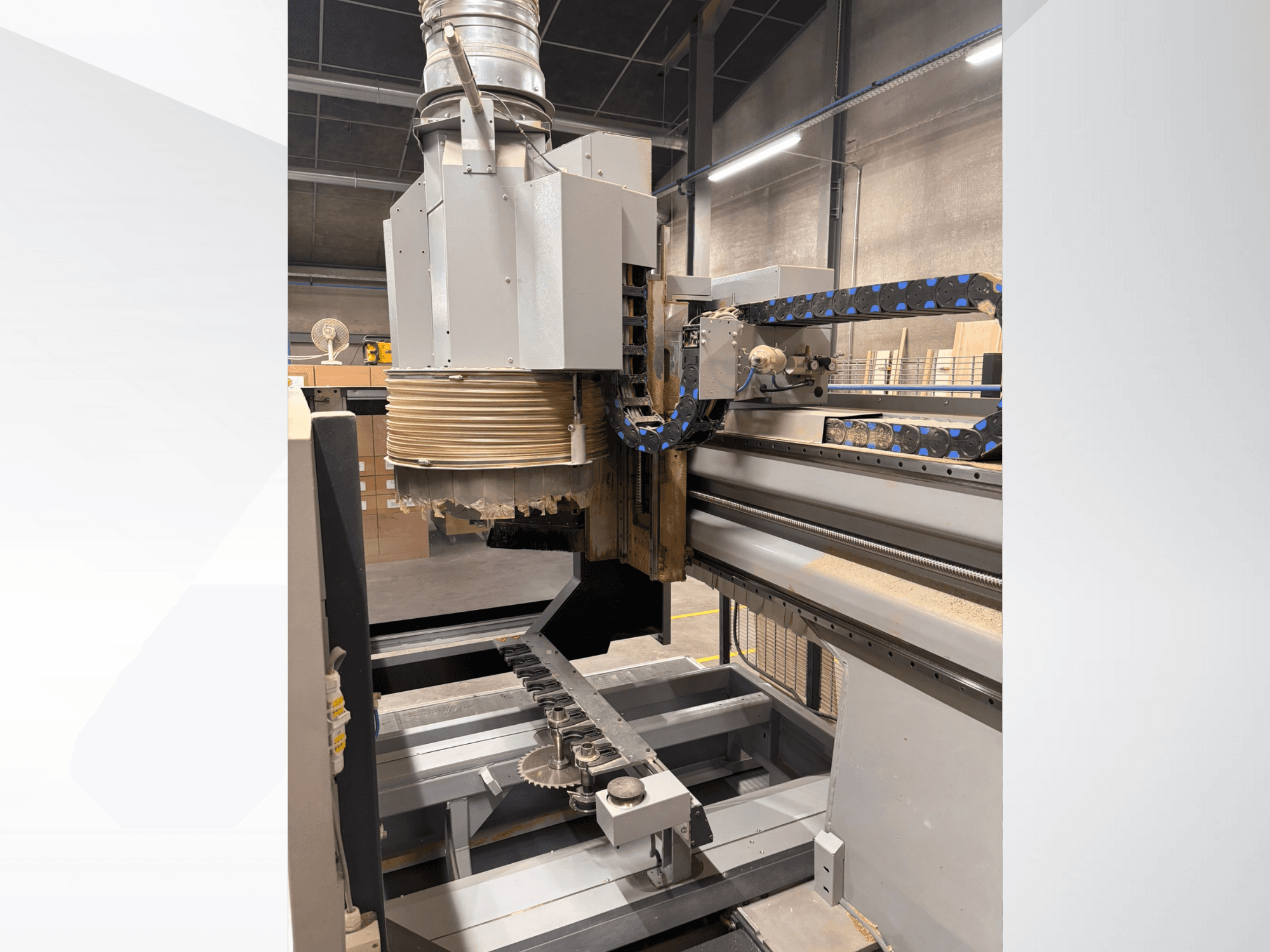 CNC-Fräsmaschine mit großer Spindel und Förderband, Seitenansicht, mit Holzbearbeitungswerkzeugen und Maschinenkomponenten.