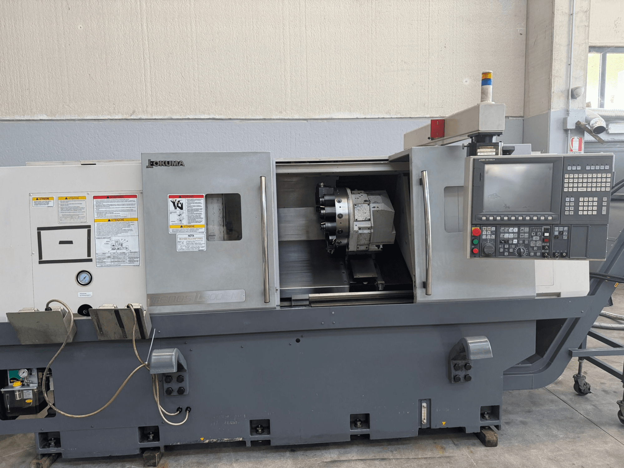 Okuma CNC-Drehmaschine, Vorderansicht, mit Bedienfeld, Werkzeughalter und Sicherheitshinweisen an der Seite.