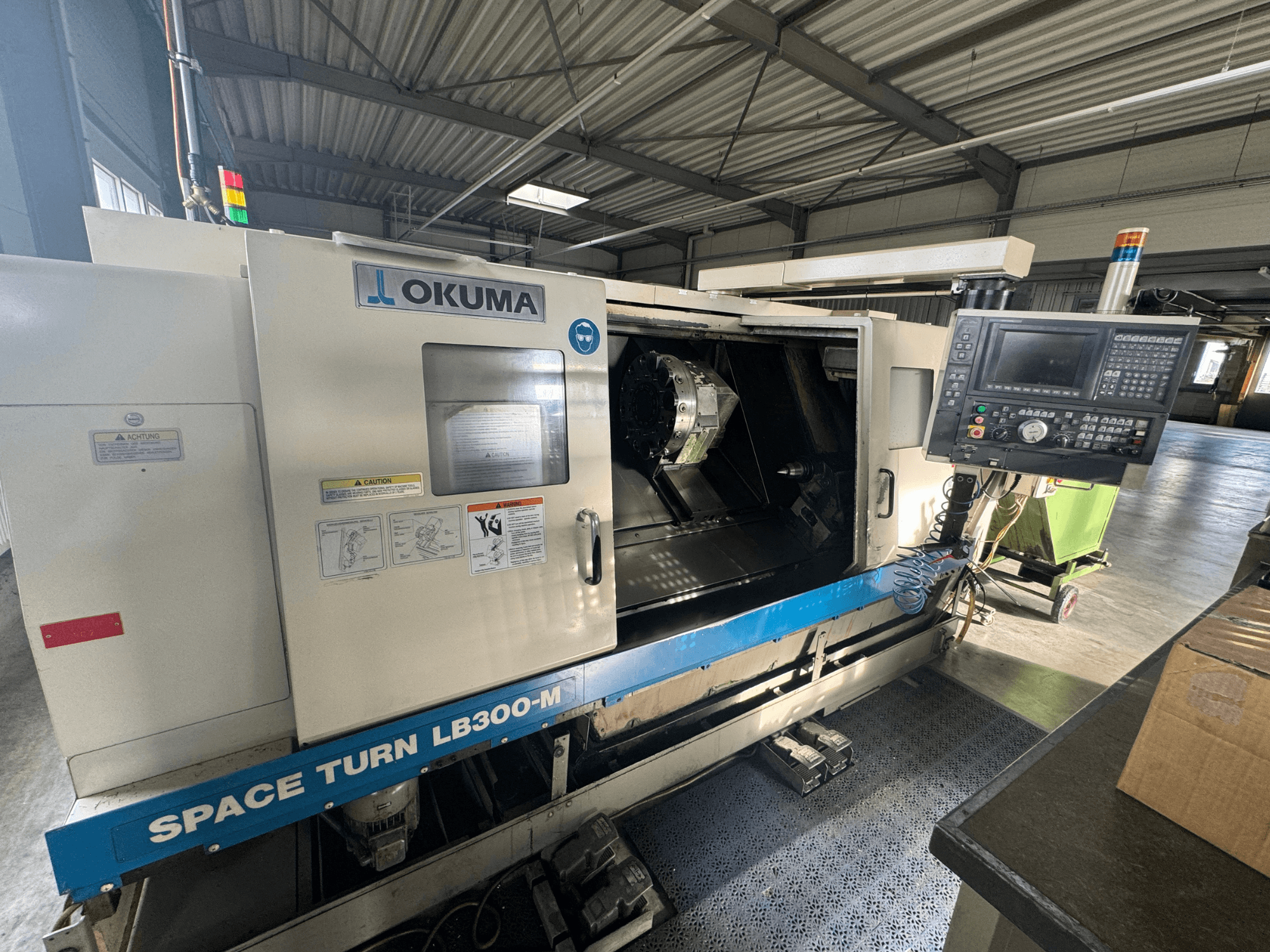 Okuma Space Turn LB300-M CNC-Drehmaschine in der Vorderansicht, mit Bedienfeld und offener Tür, die den inneren Bearbeitungsbereich zeigt.