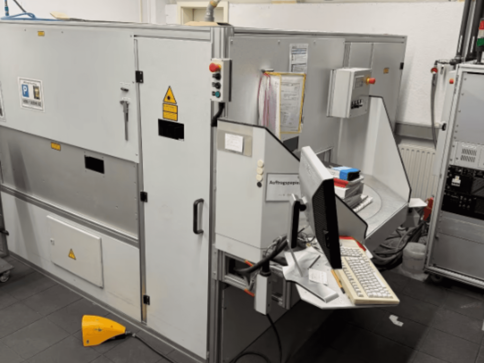 Industriemaschine mit einem Computerterminal, Seitenansicht; mit Bedientasten und Sicherheitswarnschildern.