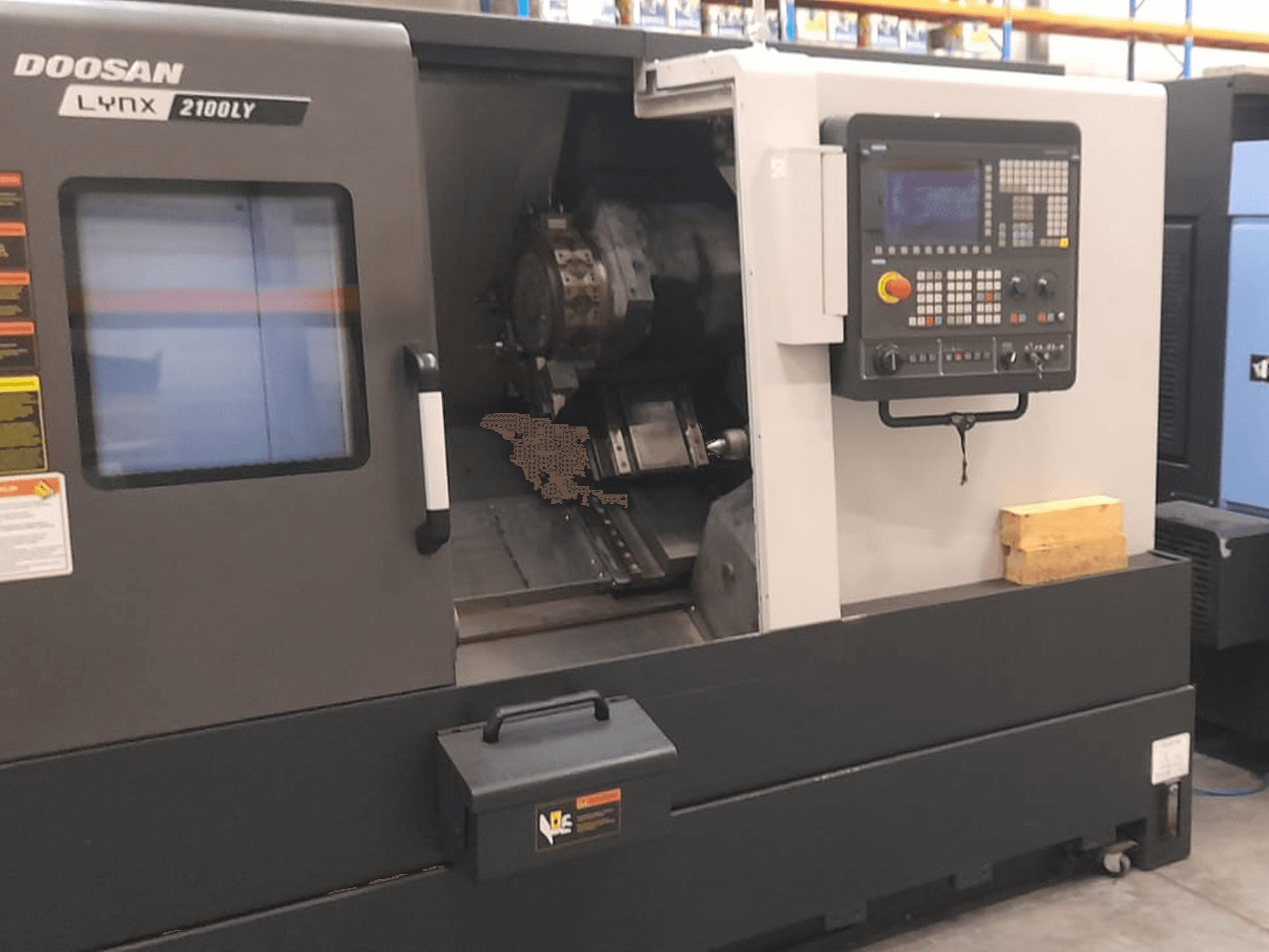 Doosan Lynx 2100LY CNC-Drehmaschine, Vorderansicht mit Bedienfeld, Werkzeughalter und innerem Arbeitsbereich; technische Etiketten sichtbar.