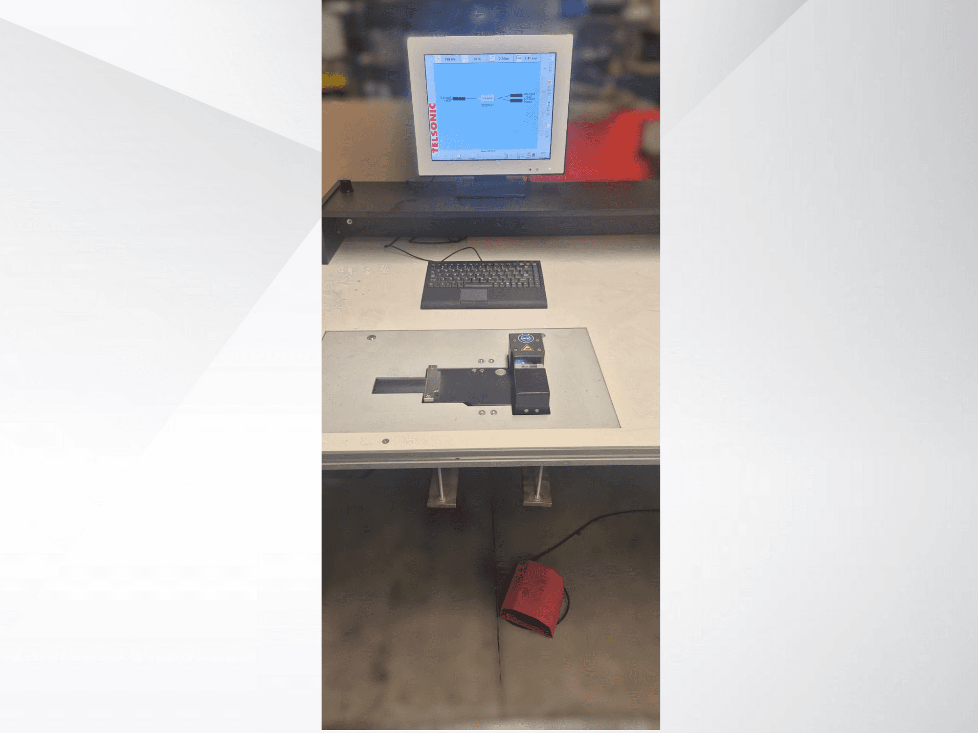 Draufsicht auf einen Prüfplatz mit Computermonitor, Tastatur und Bedienfeld mit einer Taste und einem grünen Licht.