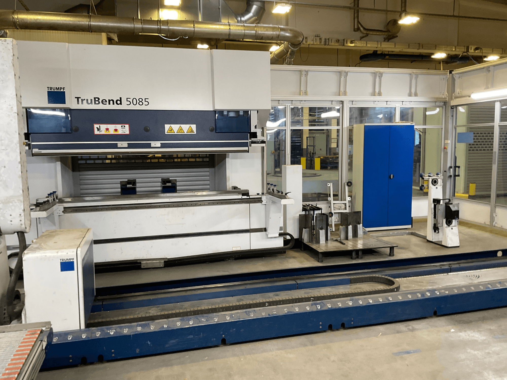 TruBend 5085 von TRUMPF, Seitenansicht einer großen Metallbiegemaschine mit Bedienpult und verschiedenen Werkzeugen daneben.