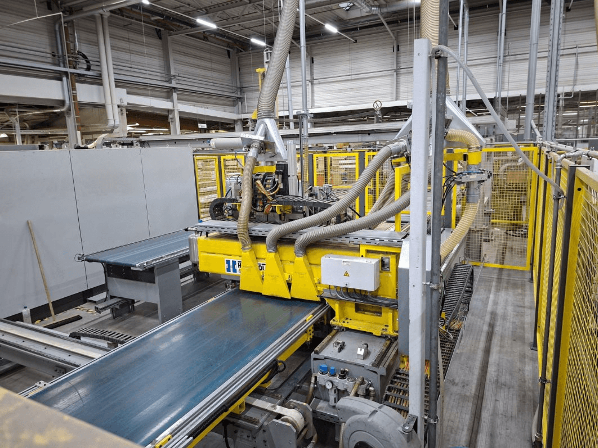 Industrielles Fördersystem aus der Seitenansicht, mit gelben Maschinen, Schalttafel und Schlauchanschlüssen für die Fertigung.