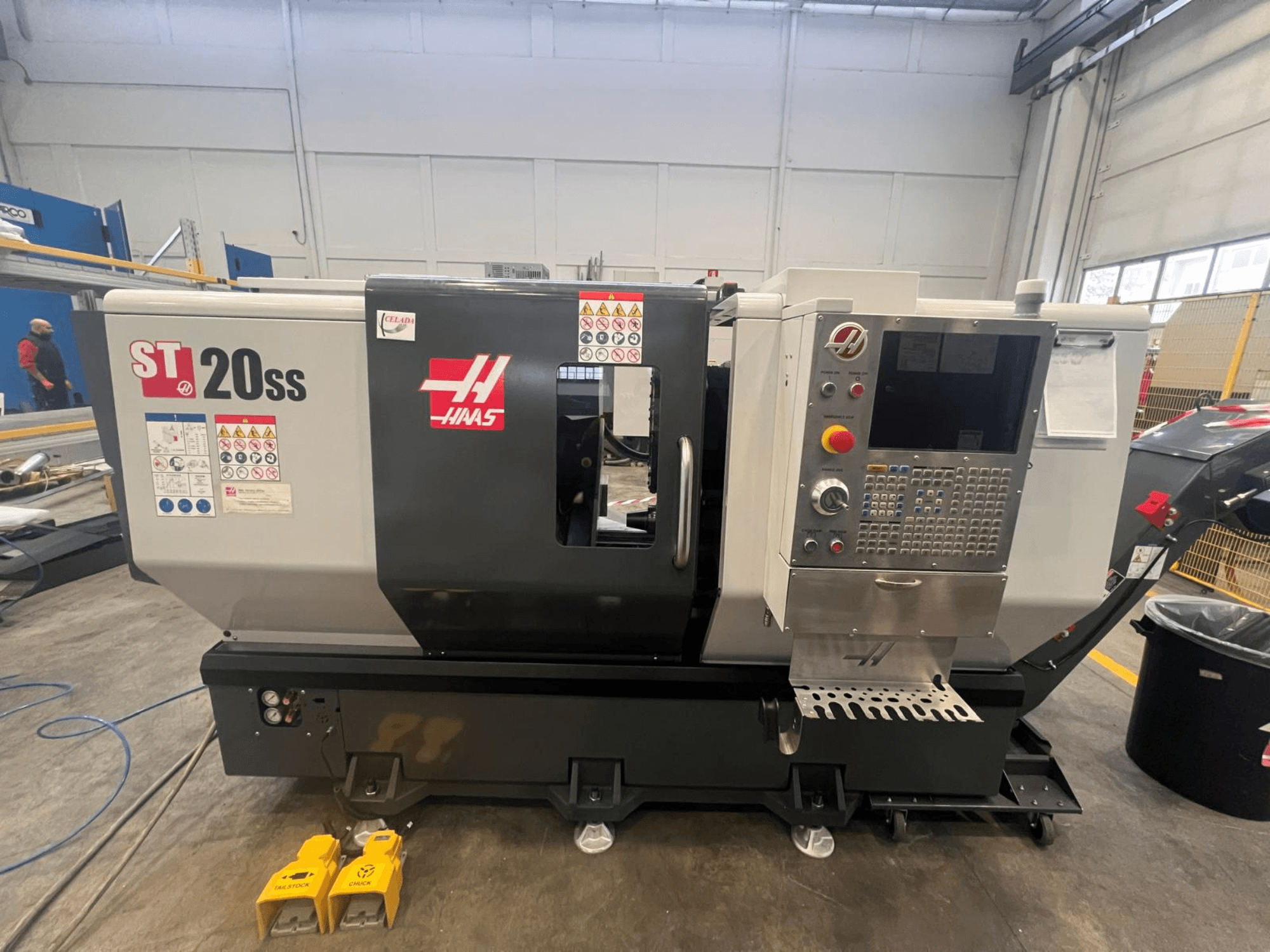 Haas ST 20SS CNC-Drehmaschine in der Seitenansicht, mit Bedienfeld, Sicherheitsschildern und Fußpedalen auf dem Boden.