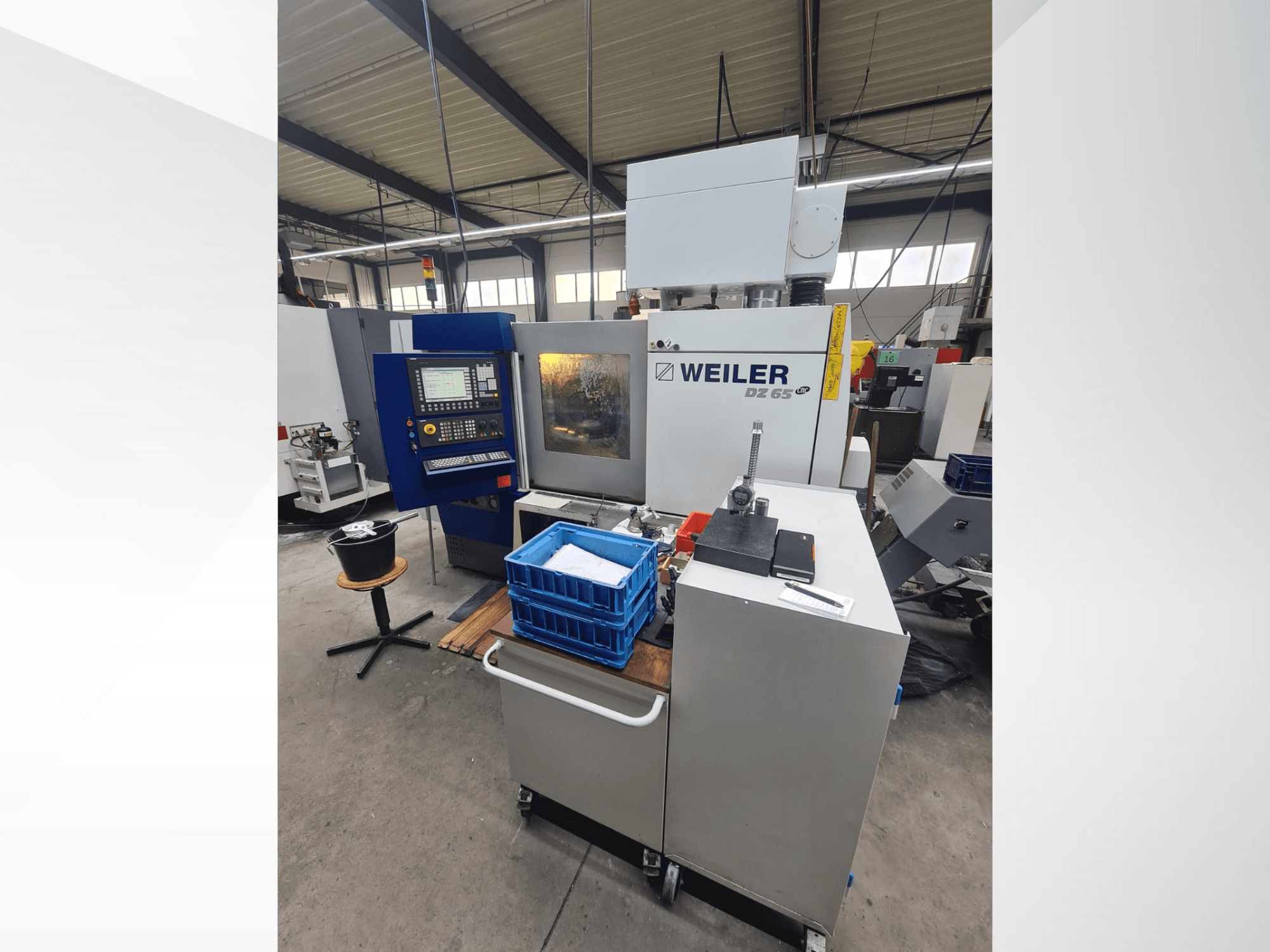 Weiler DZ 65 CNC-Maschine in einer Werkstatt, Vorderansicht mit Bedienfeld, Werkzeugen und blauen Ablagefächern sichtbar.