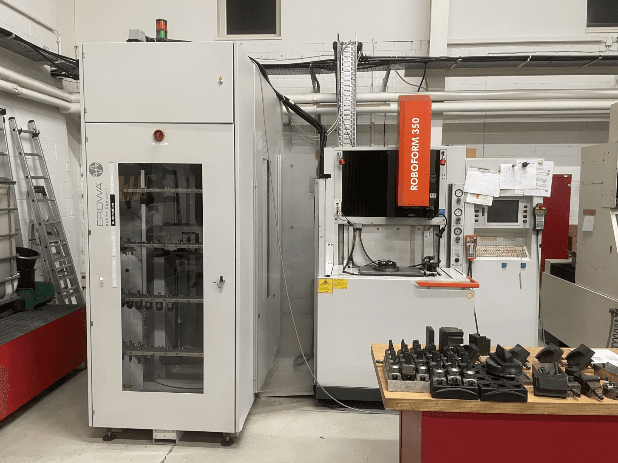 Senkerodiermaschine CHARMILLES Roboform 350, Vorderansicht, mit Werkzeugen auf einem Tisch und angrenzenden Geräten.