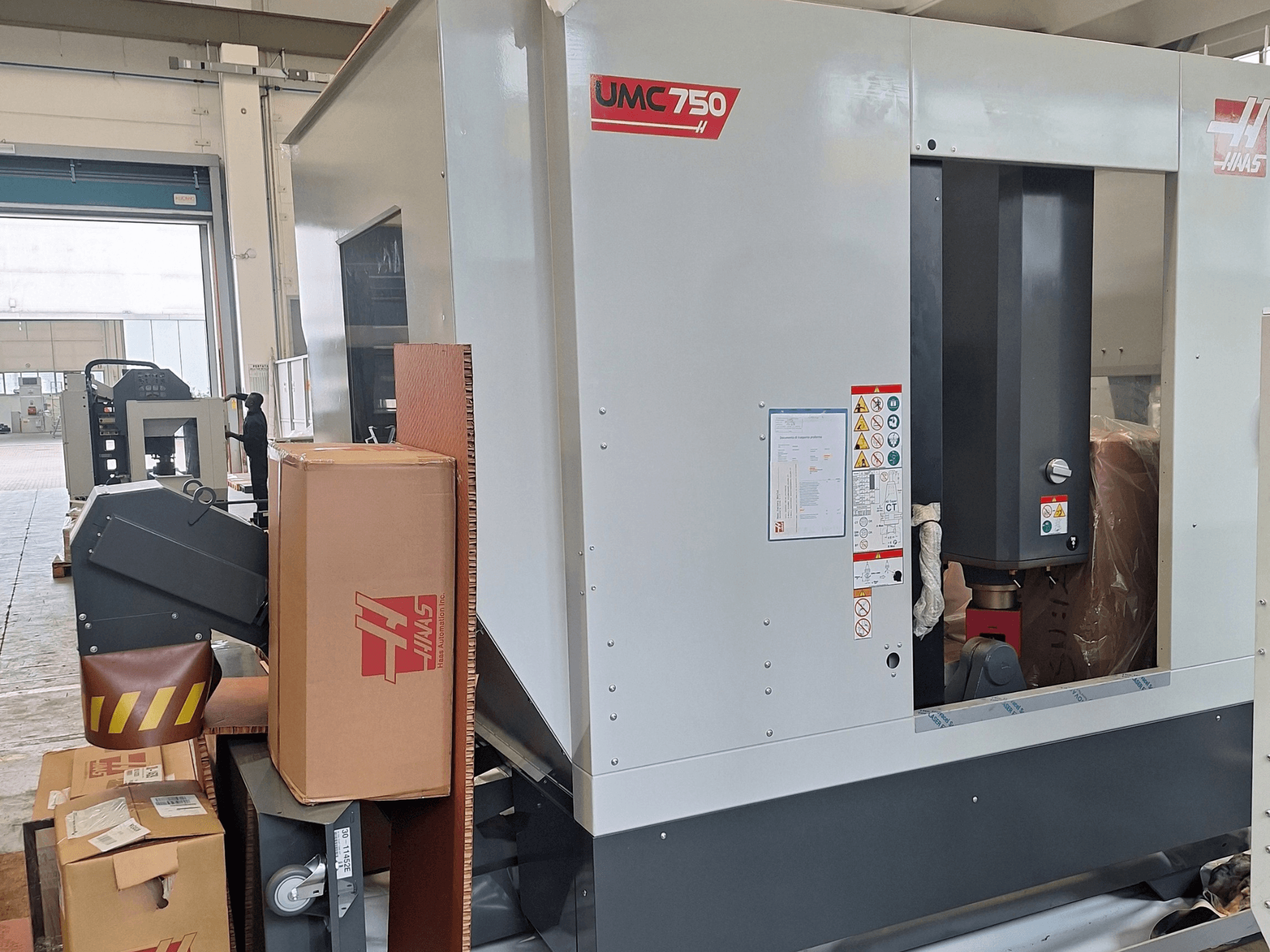 HAAS UMC-750 Universal-Bearbeitungszentrum, Seitenansicht, mit Blick auf das Bedienfeld und den Werkzeugmagazin sowie Warnschilder und Verpackung.