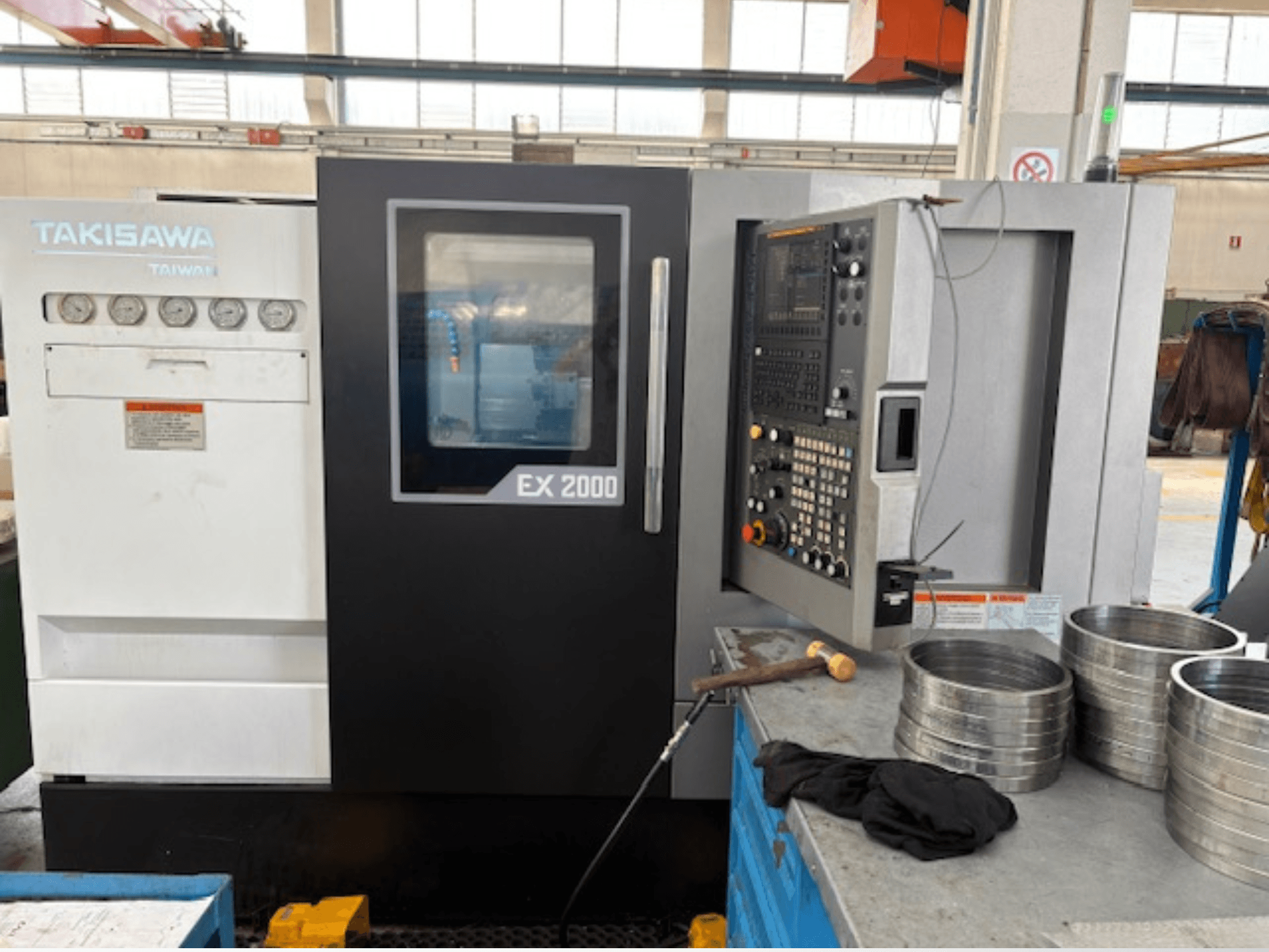 Takisawa EX 2000 CNC-Maschine, Vorderansicht, mit Bedienfeld, Messgeräten und Metallteilen auf einem Werkstatttisch.