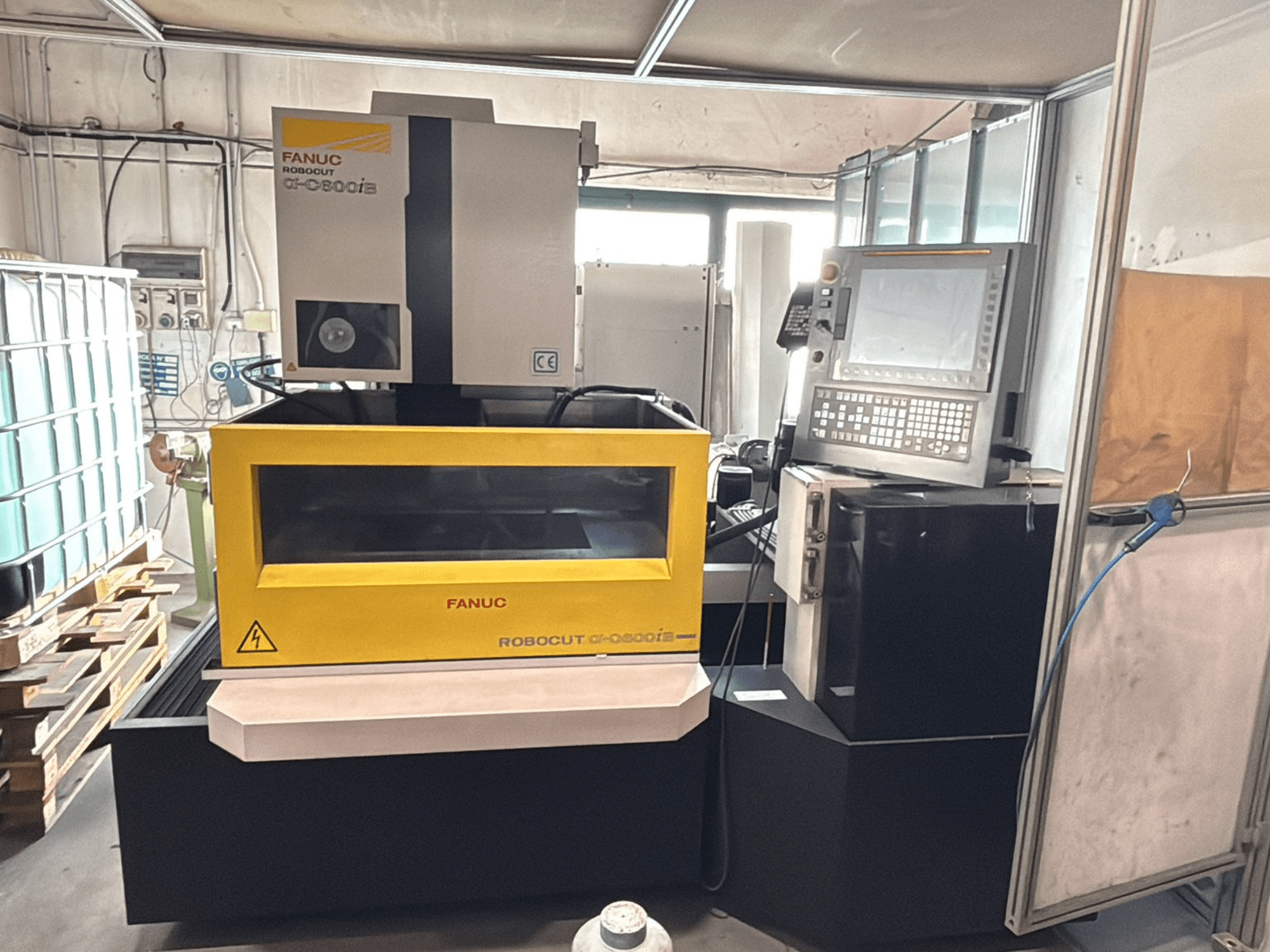 Vorderansicht einer FANUC Robocut α-0iE CNC-Maschine mit einem gelben Gehäuse, auf dem das Bedienfeld und das Display zu sehen sind.
