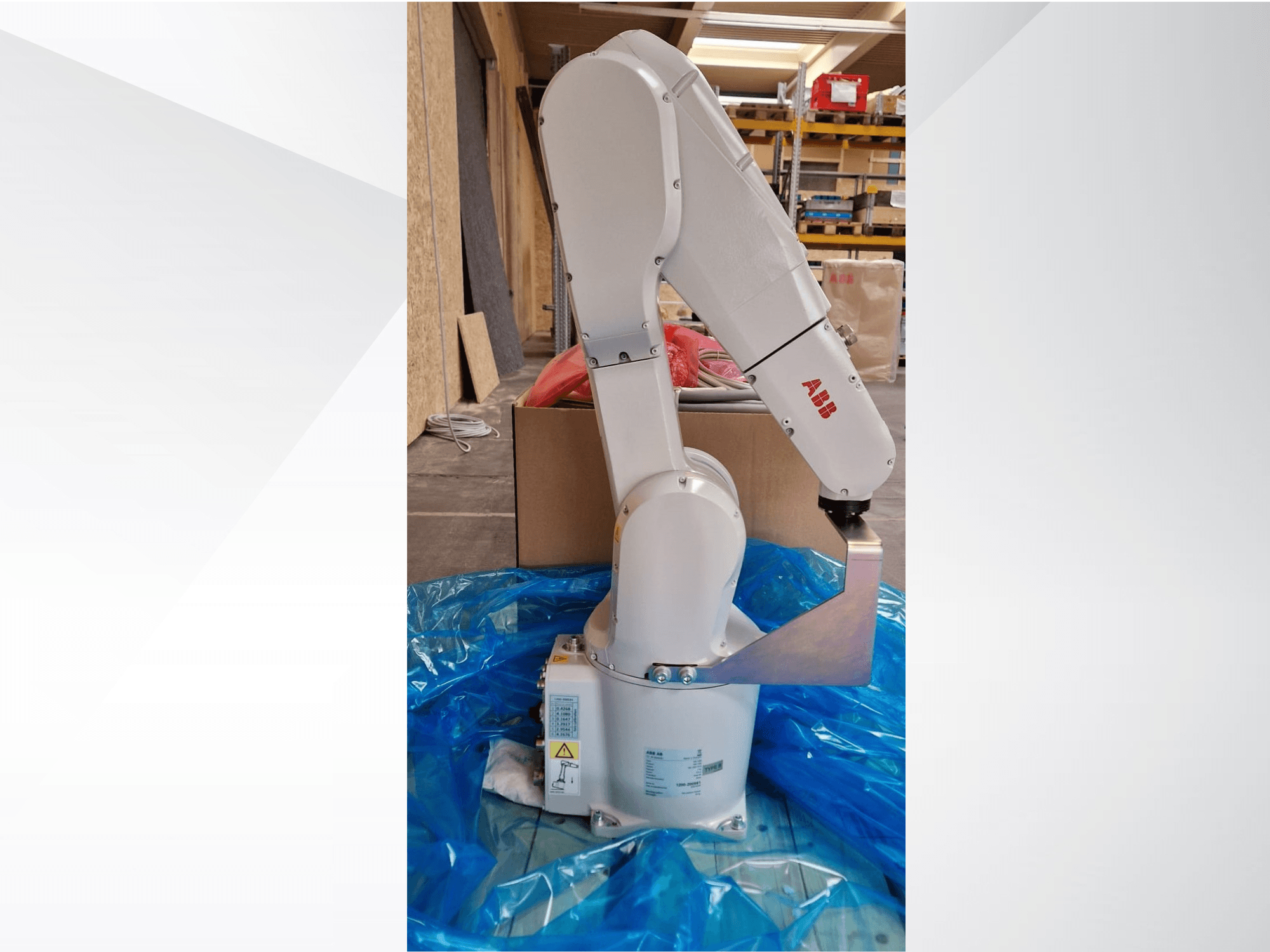 ABB-Roboterarmmodell, Seitenansicht auf blauer Plane, mit Gelenken und Metalleffektor, mit sichtbaren technischen Etiketten.