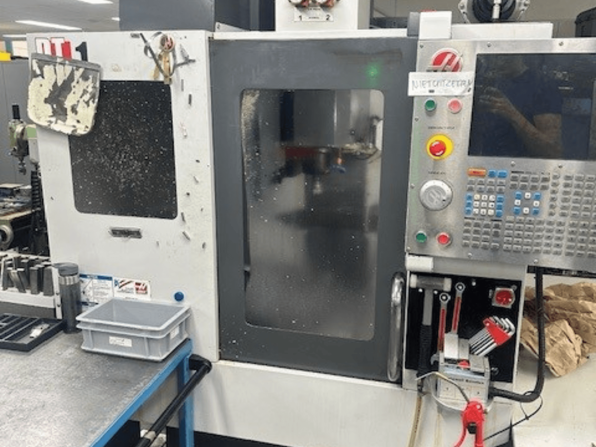 Haas DT-1 Vertikal-Bearbeitungszentrum, Vorderansicht mit Bedienfeld, sichtbarem Schmutz und Werkzeugablage auf der Werkbank.