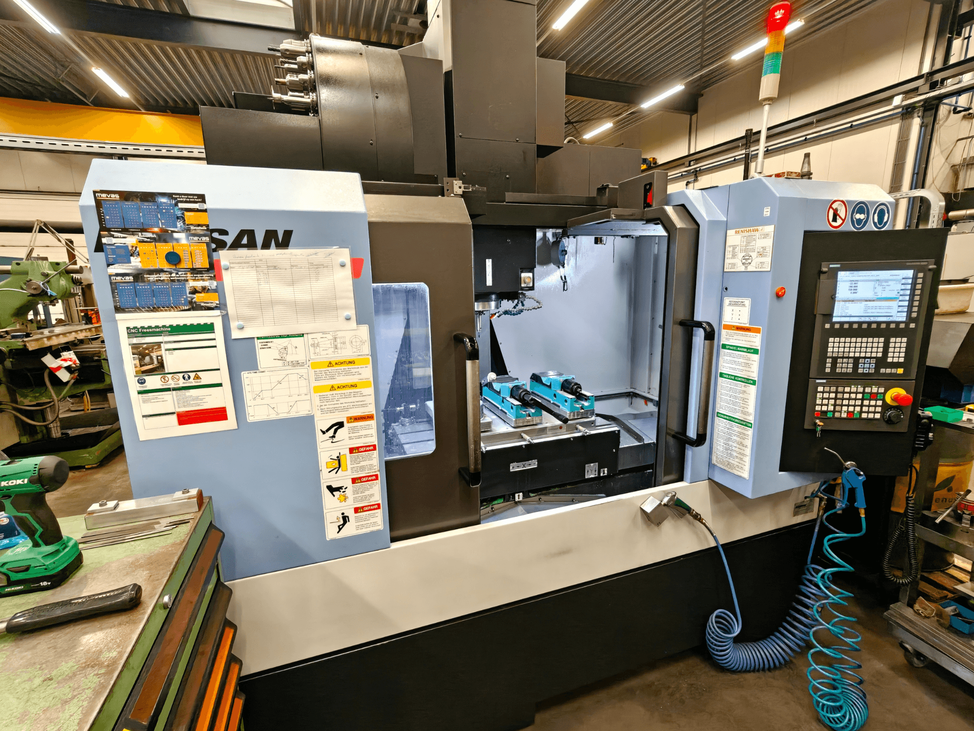Vertikales Bearbeitungszentrum DOOSAN DNM 400 II in einer Werkstatt, mit Bedienelementen, Werkzeughaltern und Sicherheitsschildern, Vorderansicht.